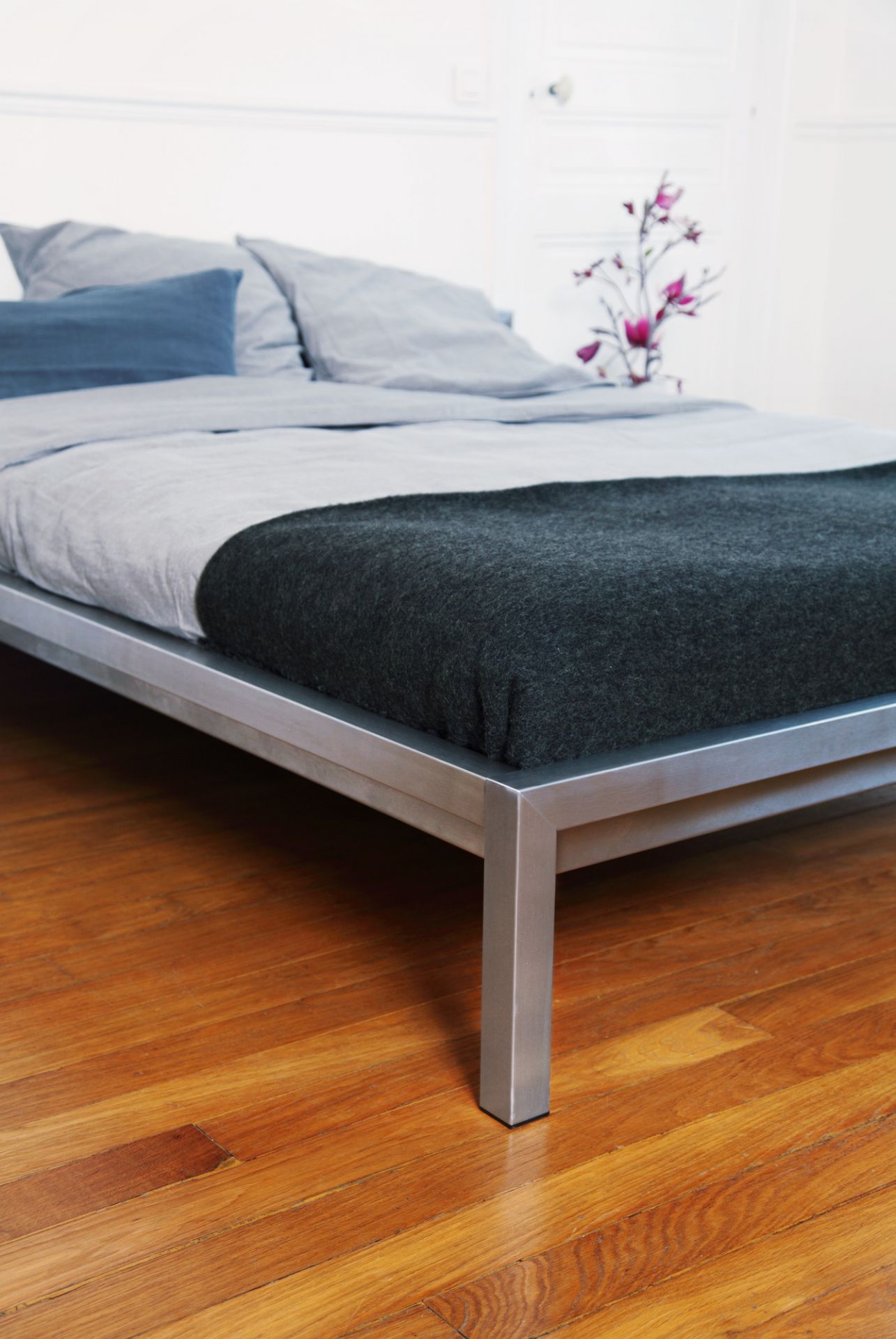 Hans Hansen Pure Bett Edelstahl, 140x200 cm, mit Bettwäsche und Decke auf Holzboden.