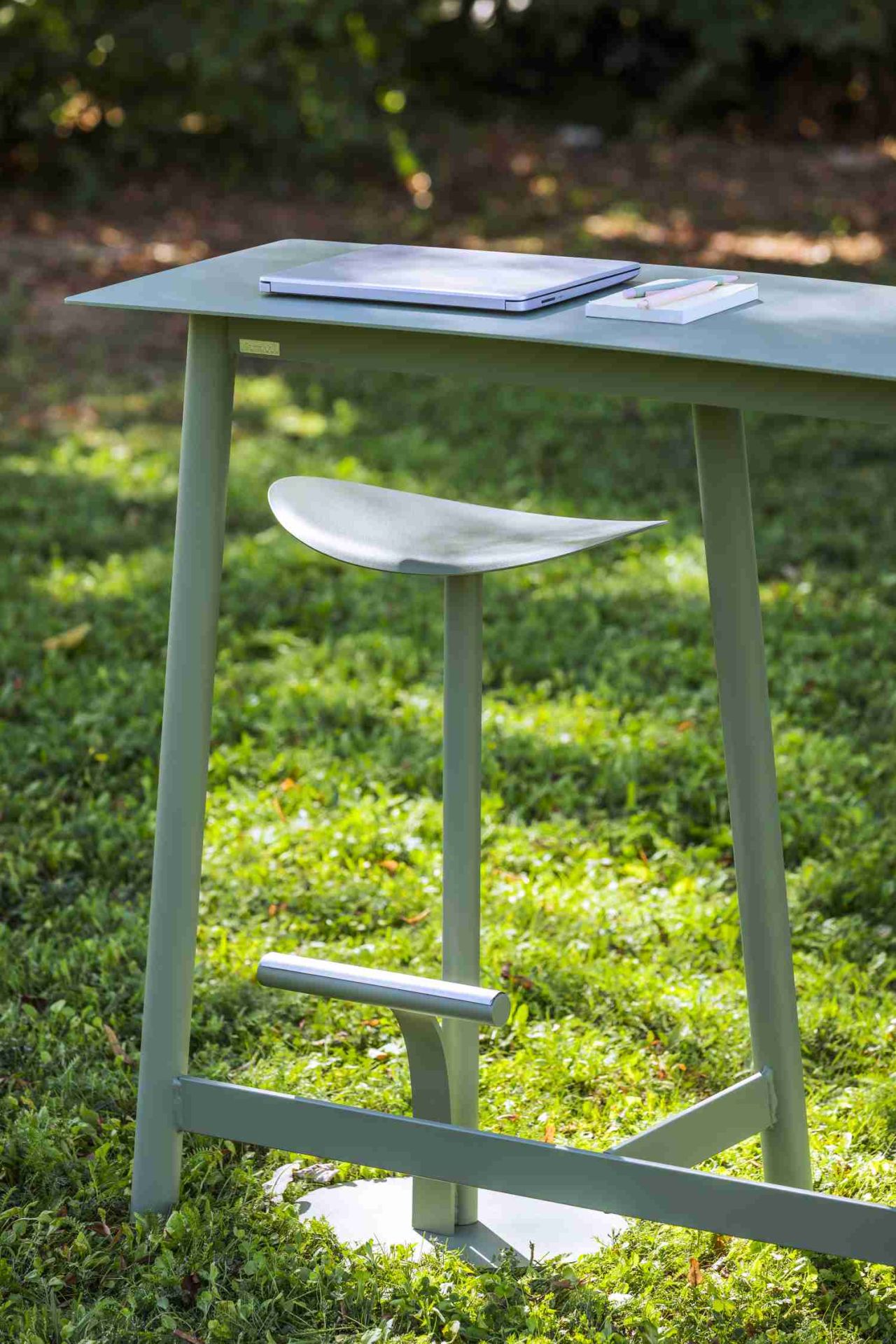 Grüne Fermob Bolder Outdoor Theke mit Hocker auf Rasen. Laptop und Notizblock liegen auf der Theke.