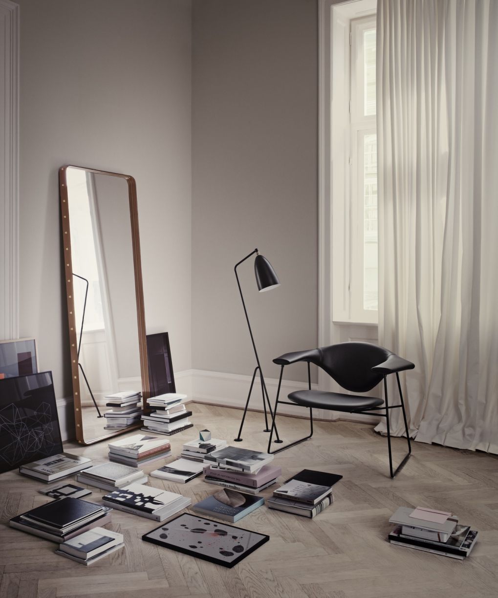 Adnet Spiegel mit braunem Lederrahmen von Gubi, stehend im Raum mit Büchern und Design-Lampe.