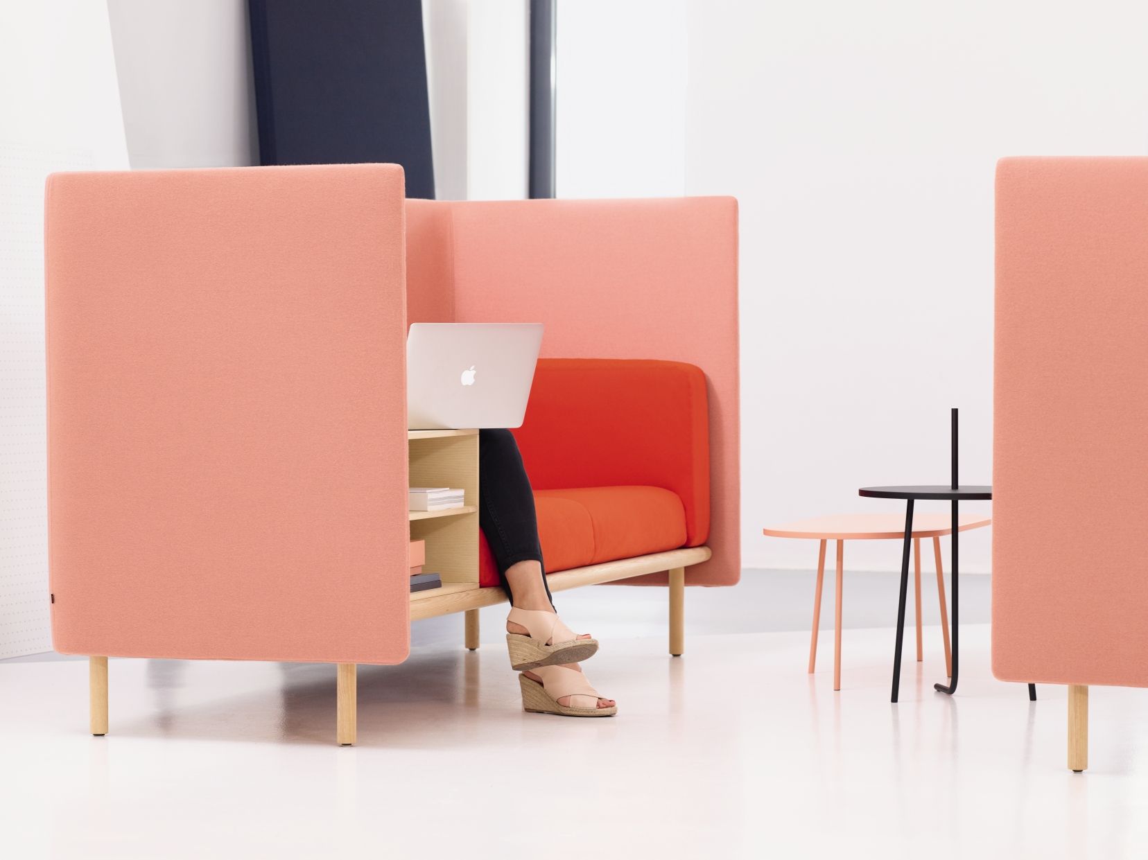 Frau arbeitet am Laptop im Cor Floater Sofa mit Trennwänden in Rosa und Orange.