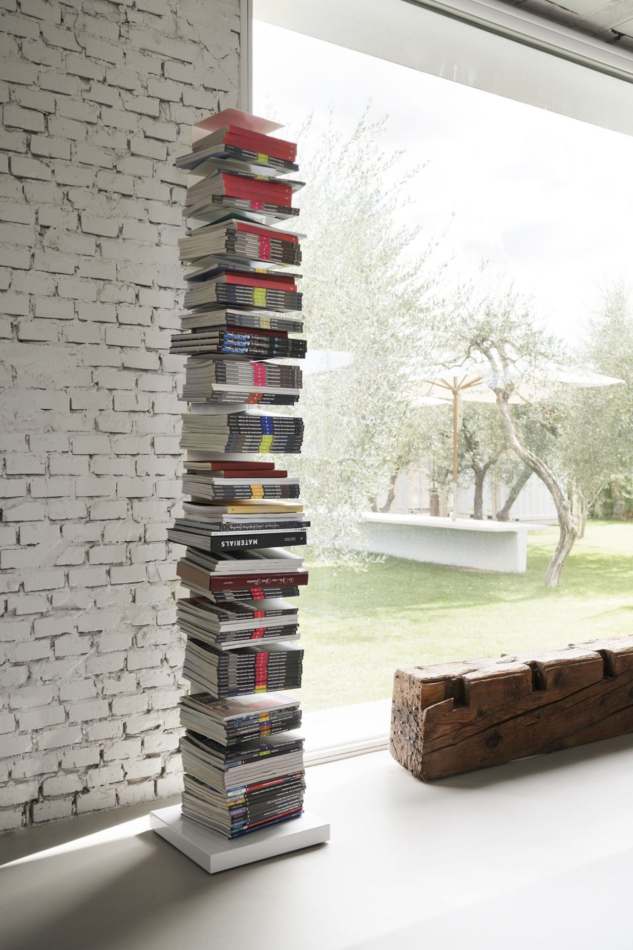 Freistehendes Ptolomeo Bücherregal mit Büchern vor Fenster und Ziegelwand. Design Bücherregal.