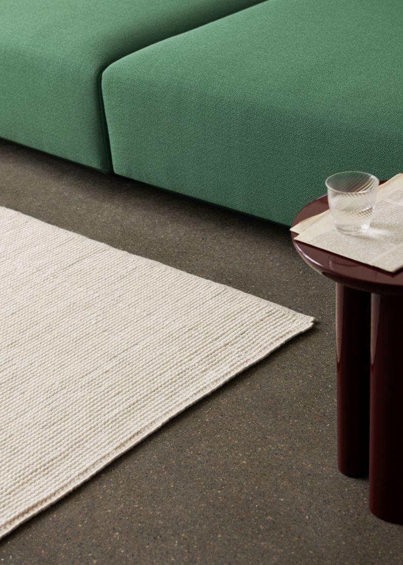 Detailaufnahme des AndTradition Collect Rug Teppichs in Creme, neben einem grünen Sofa und Beistelltisch.