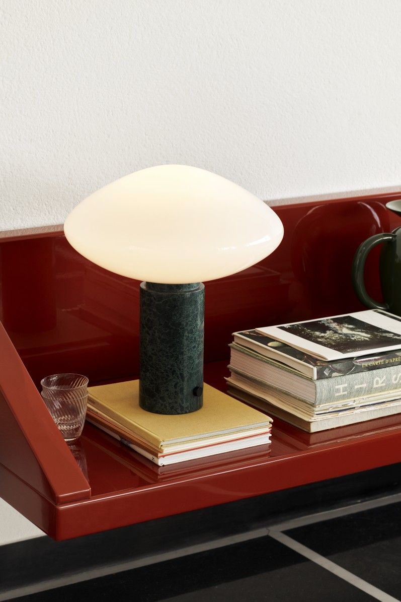 AndTradition Mist AP17 Tischleuchte Guatemale Verde auf rotem Regal mit Büchern und Glas.