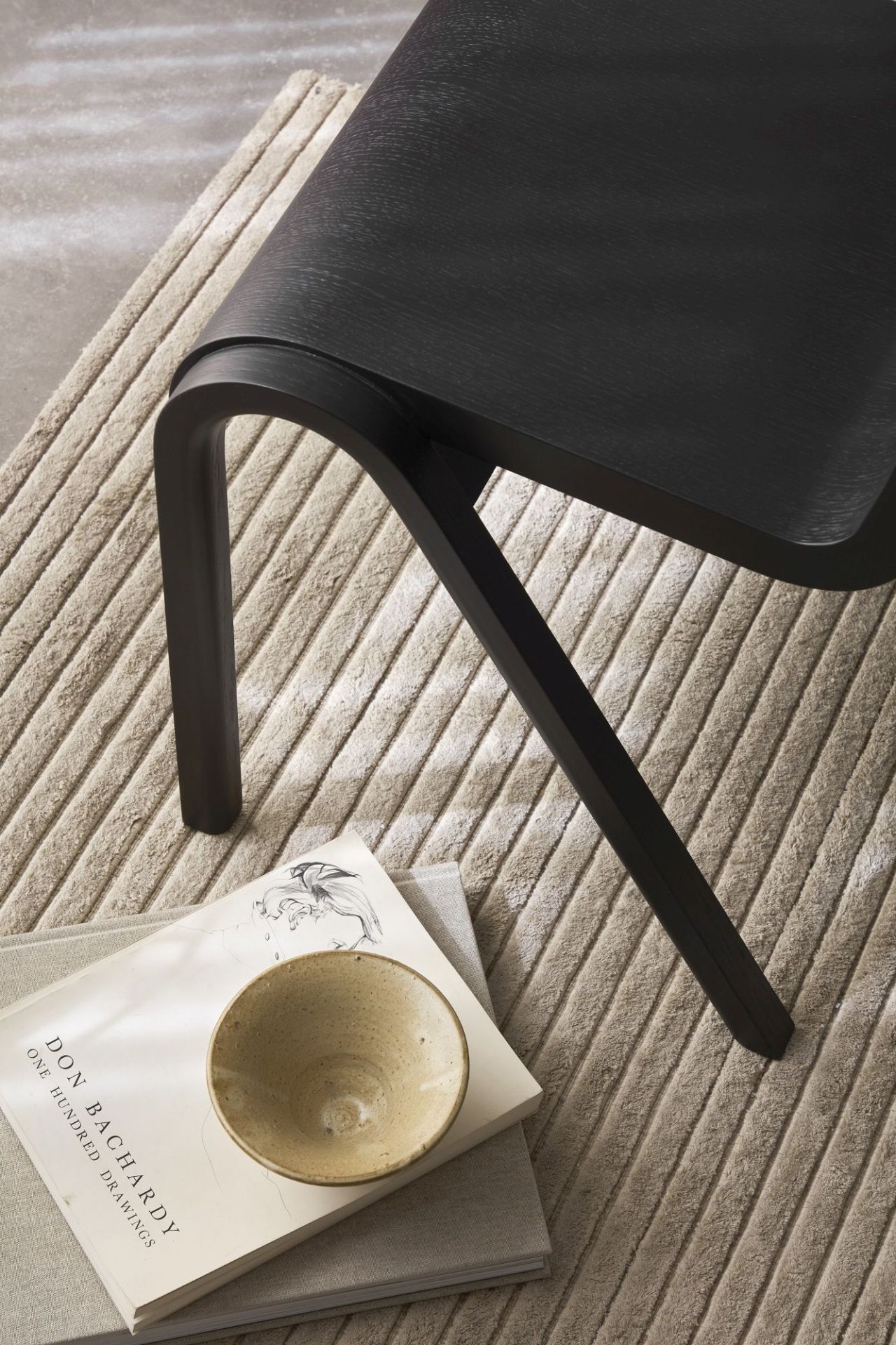Detailaufnahme vom Ready Dining Chair Holzstuhl von Audo Copenhagen in Schwarz, auf Teppich mit Büchern und Schale.