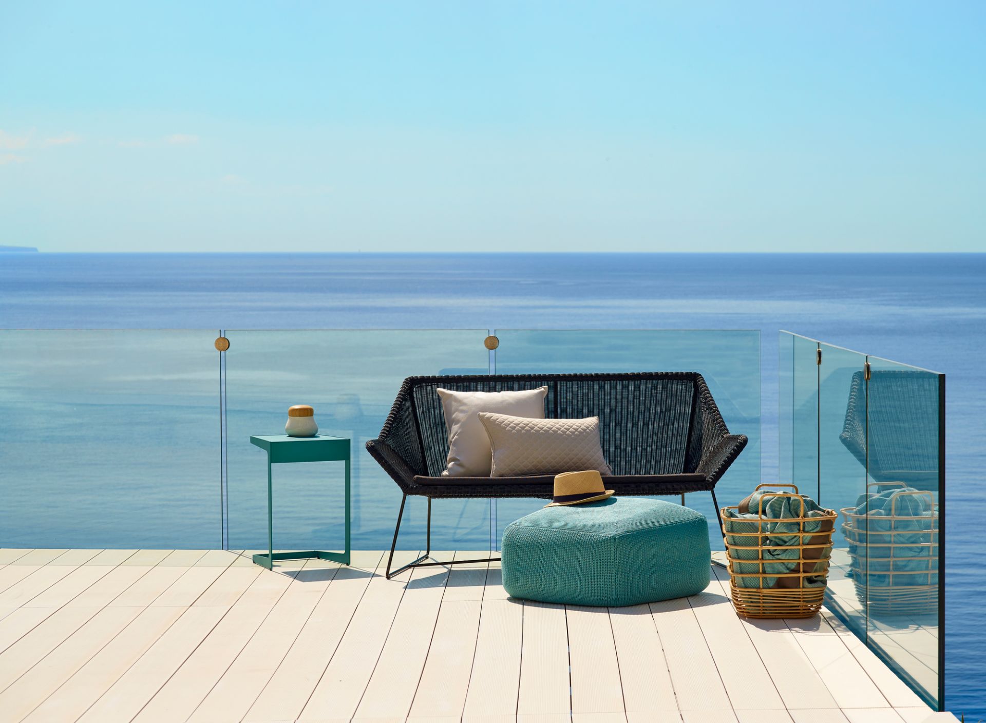 Breeze Loungesofa von Cane-Line auf Terrasse mit Meerblick. Outdoor Sofa mit Kissen und Beistelltisch.