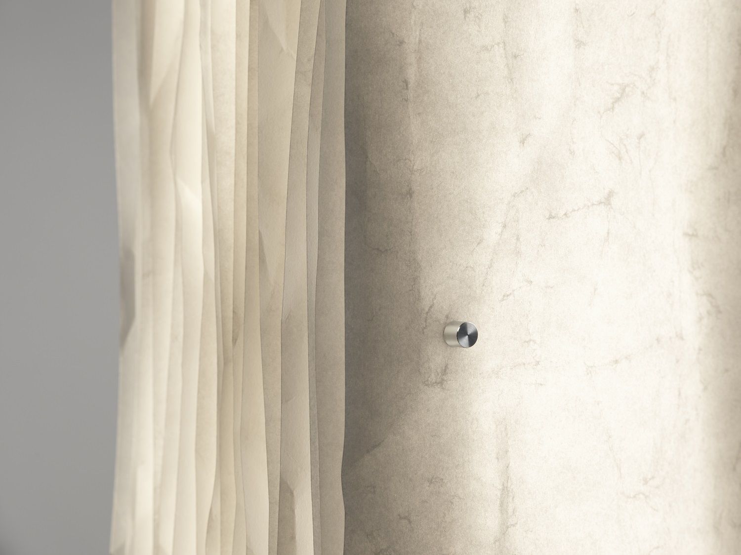 Detailaufnahme der Totem Stehleuchte: Beige Stele mit sanften Lichteffekten und silbernem Befestigungsdetail an der Wand.