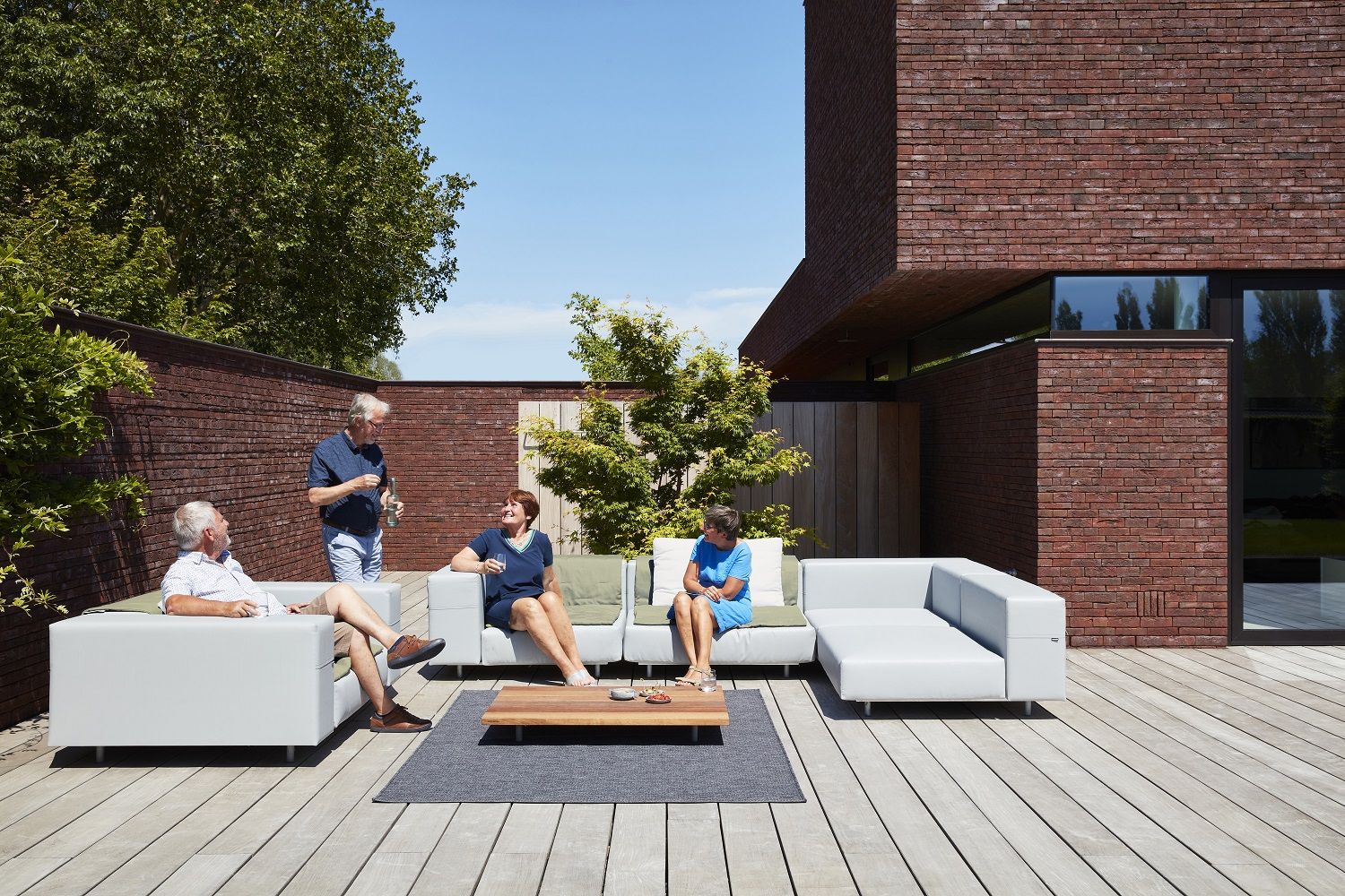 Walrus Outdoor Eckmodul von Extremis: Moderne Gartenmöbel, graues Lounge Sofa mit Personen im Außenbereich.