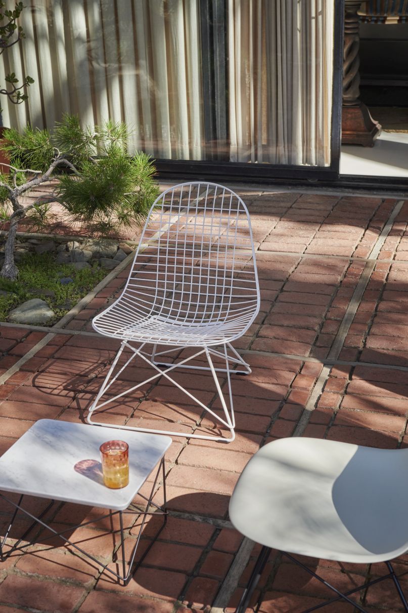 Weißer Eames Stuhl mit Drahtgestell von Vitra im Außenbereich auf Backsteinboden. Designklassiker.