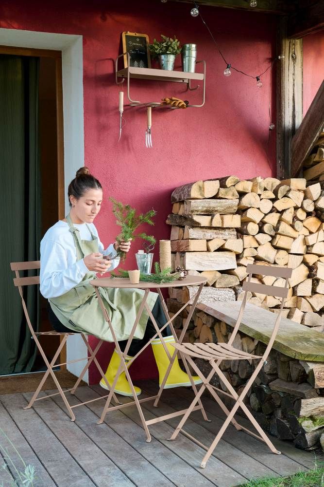 Frau am Gartentisch mit Fermob Picolino Wandregal im Hintergrund, Outdoor-Möbel für Balkon und Terrasse.