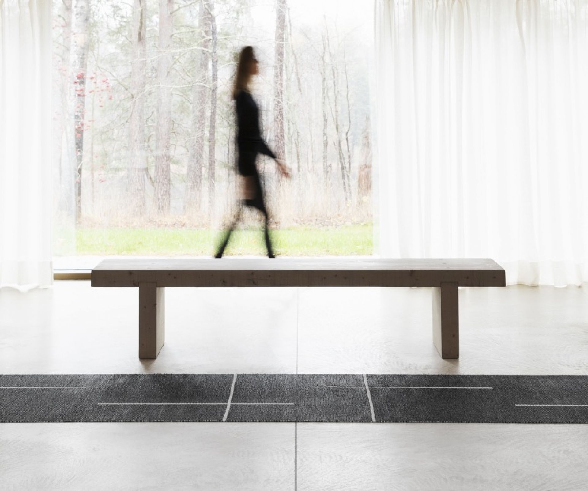 Fred Teppich Pappelina in Schwarz, 70x270 cm, unter einer Holzbank auf hellem Boden. Moderner Kunststoffteppich für Innenräume.