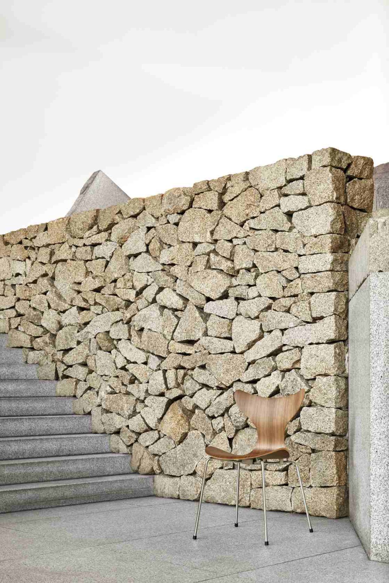 Fritz Hansen Lily Stuhl 3108 aus Holz mit Stahlbeinen vor Steinmauer.