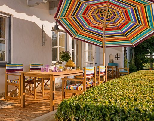 Multicolor Sonnenschirm von Weishäupl spendet Schatten über einer stilvollen Gartengarnitur mit Holztisch und Stühlen.