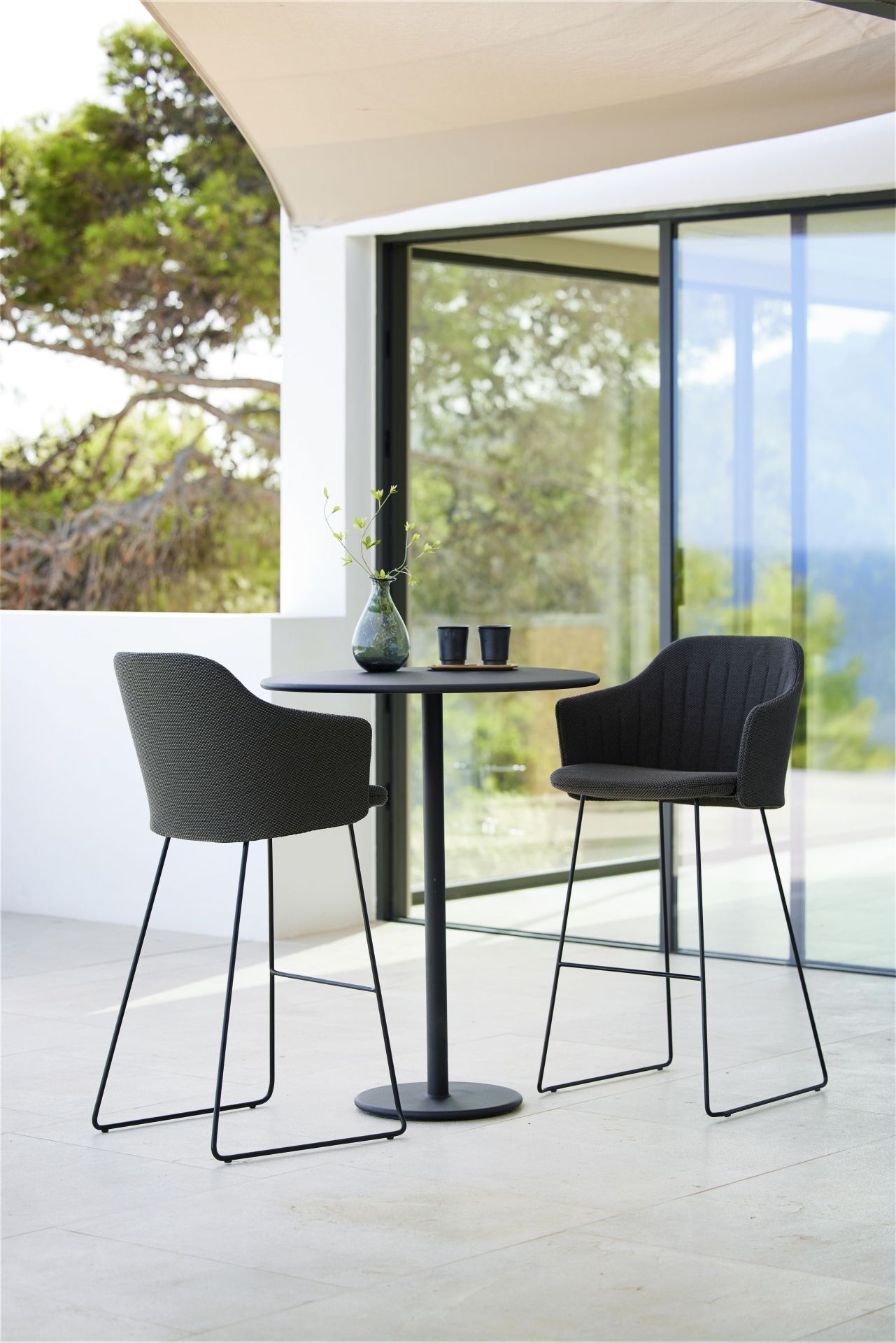 Zwei Cane-Line Choice Barhocker mit Rückenbezug und schwarzem Tisch auf einer Terrasse.