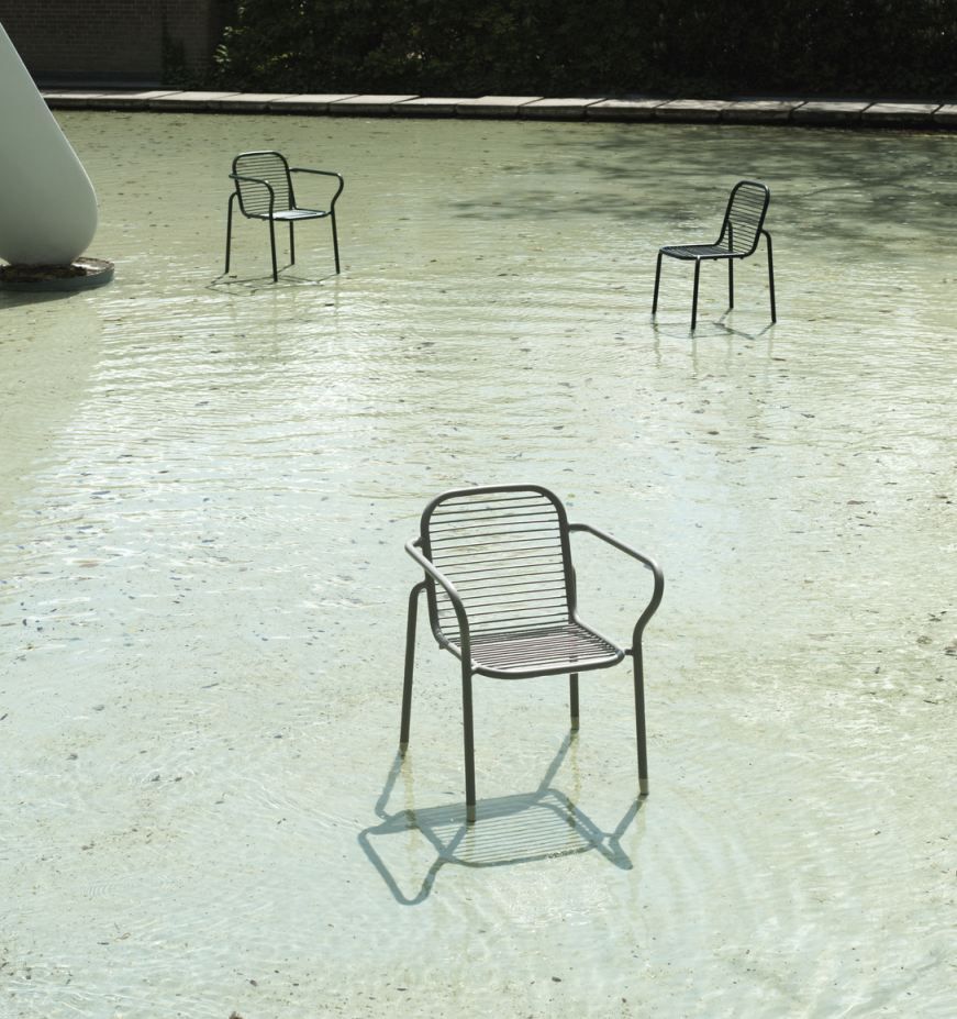 Drei schwarze Vig Chair Stühle von Normann Copenhagen stehen im flachen Wasser eines Außenbereichs.