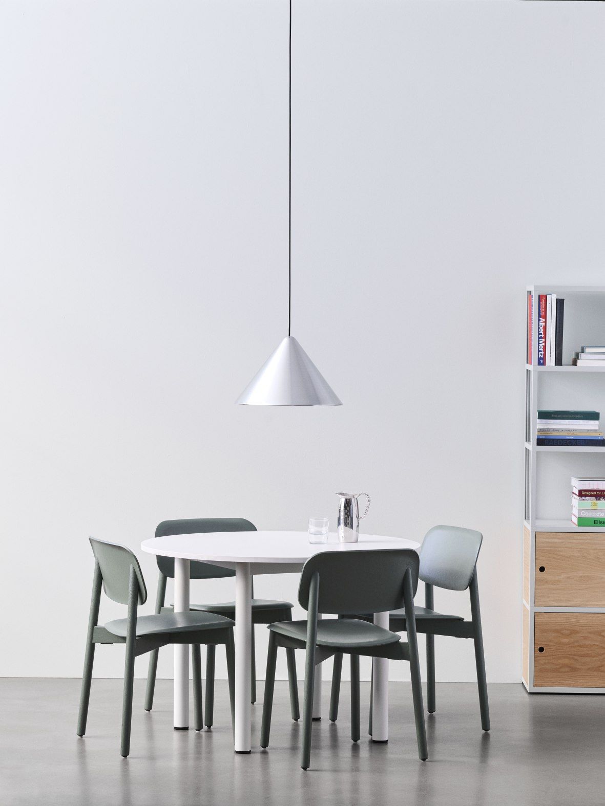 Heller Raum mit Hay Annex Table Round Esstisch, vier grünen Stühlen, Lampe und Regal.