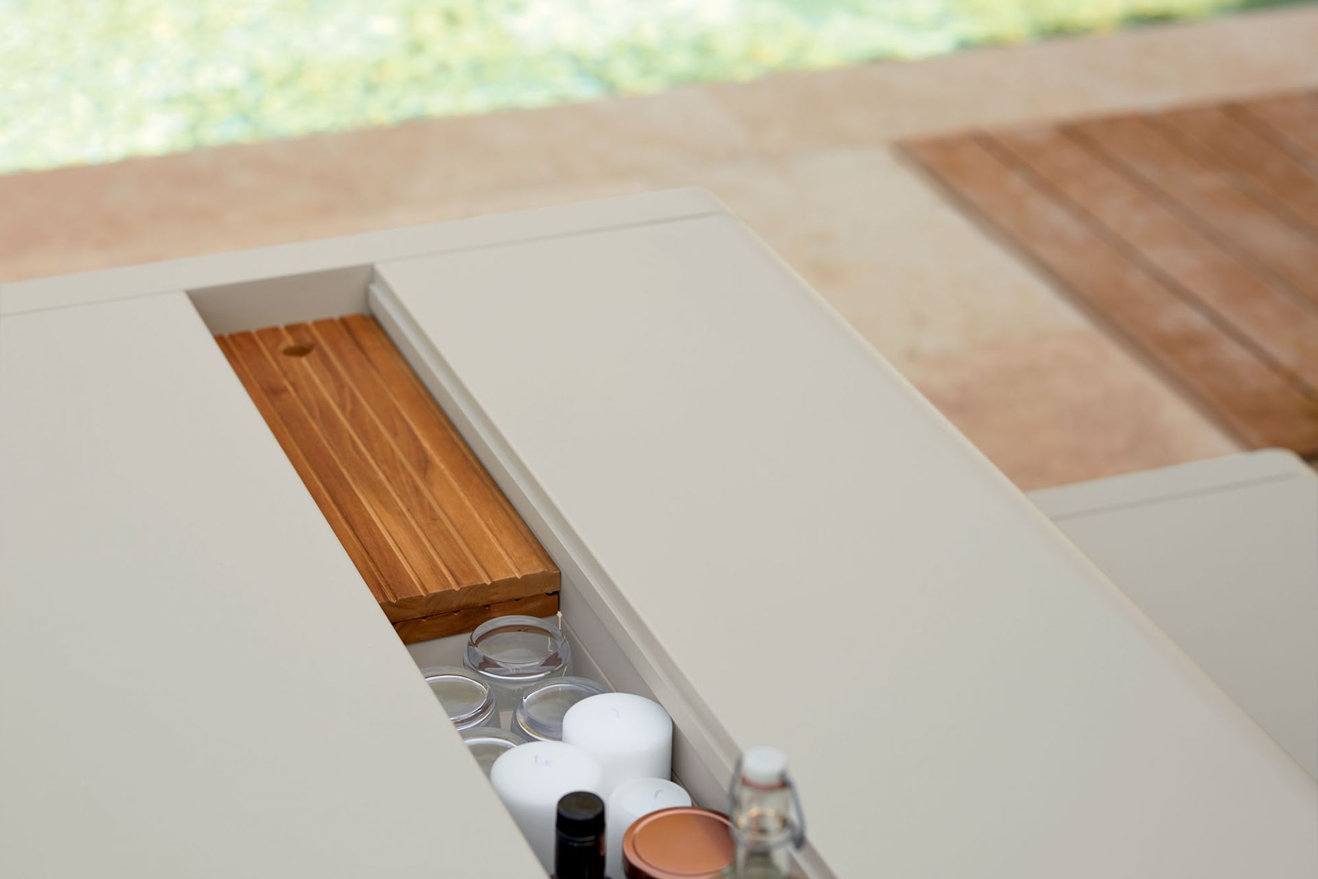 Detailaufnahme des Fermob Bellevie Outdoor Tisches mit integriertem Stauraum für Gläser, Kerzen und einer Holzplatte.