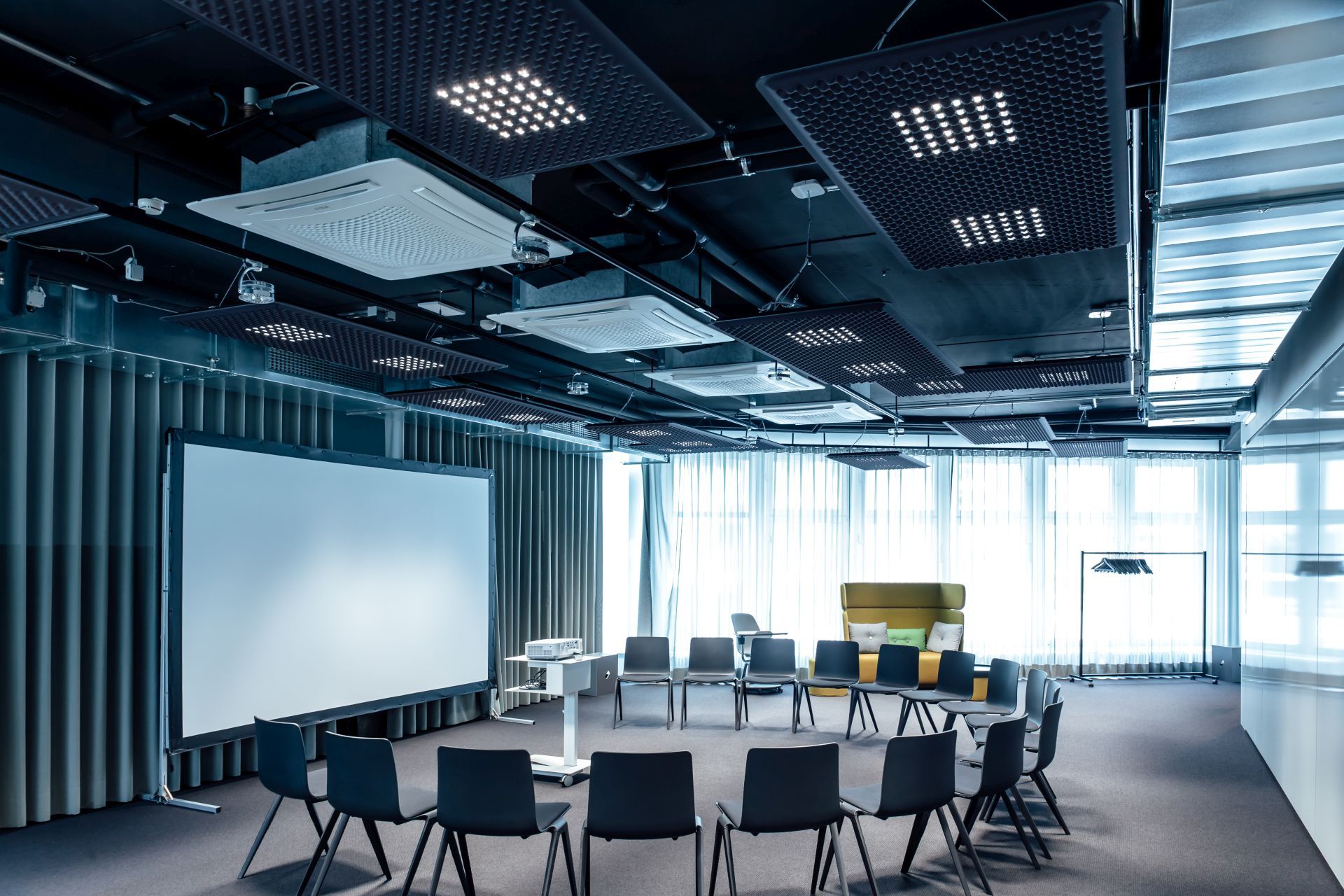 Moderner Konferenzraum mit Stühlen im Kreis, Leinwand, Projektor und Akustikdecken für Präsentationen und Schulungen.