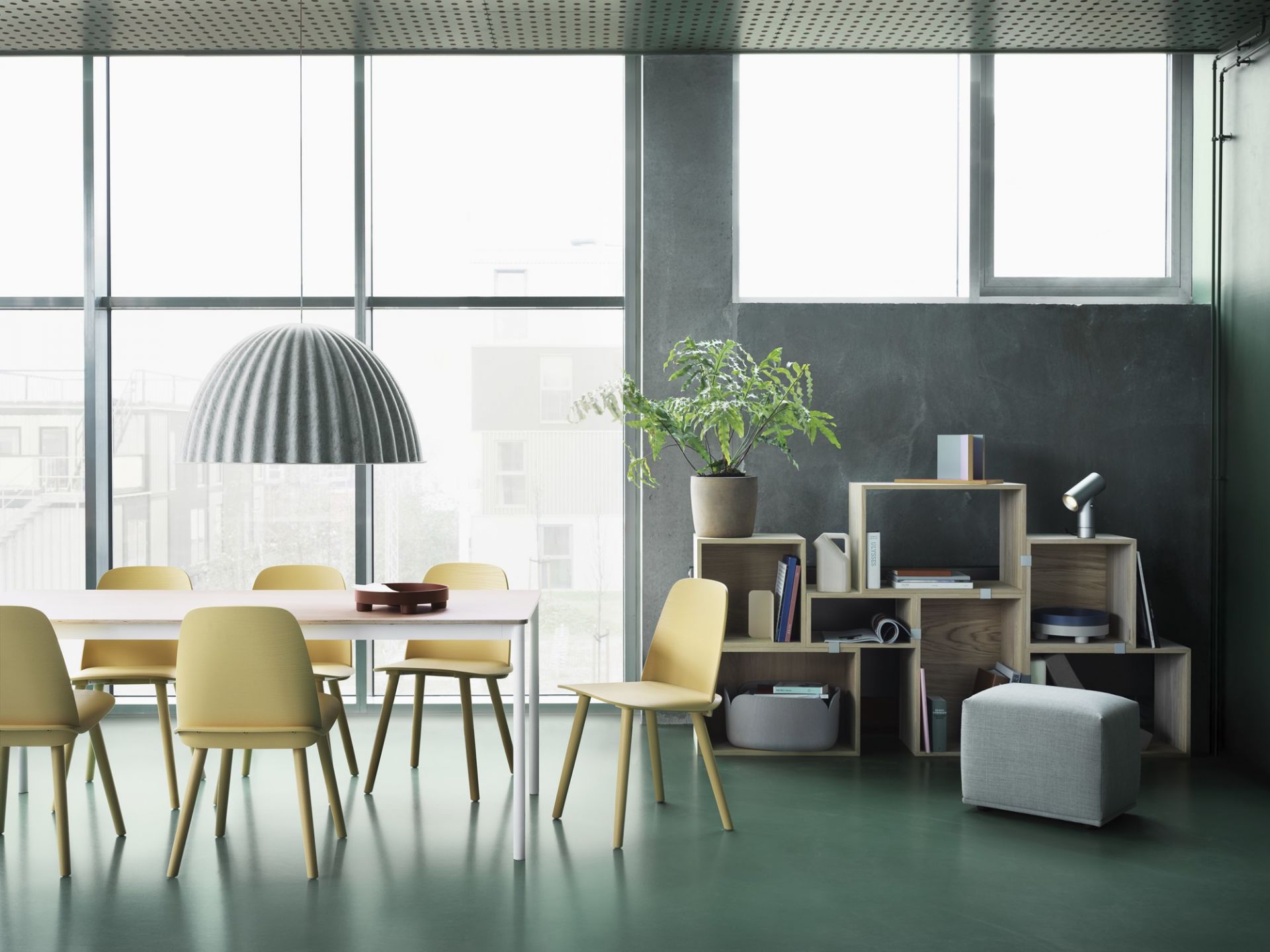 Helle Esszene mit Muuto Under The Bell Pendelleuchte, gelben Stühlen und modernem Regal.