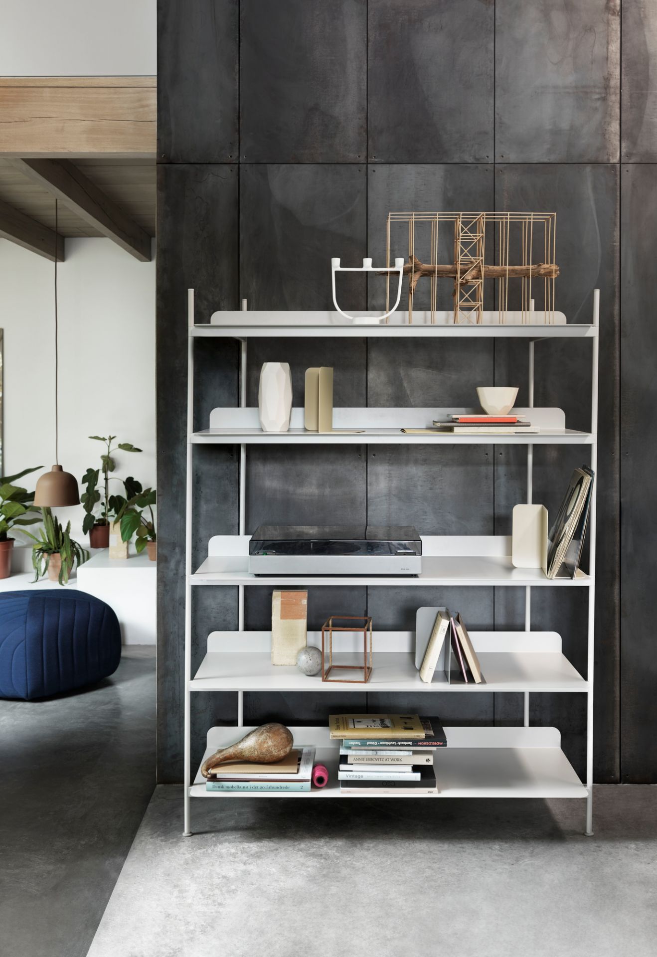 Muuto Compile Regalsystem in Weiß, verschiedene Höhen, dekoriert mit Büchern und Deko-Objekten vor dunkler Wand.