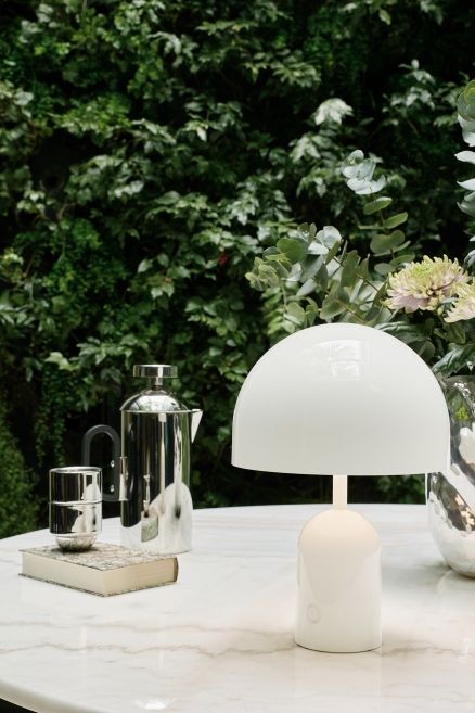 Weiße Bell Portable LED Tischleuchte von Tom Dixon auf einem Tisch im Freien.