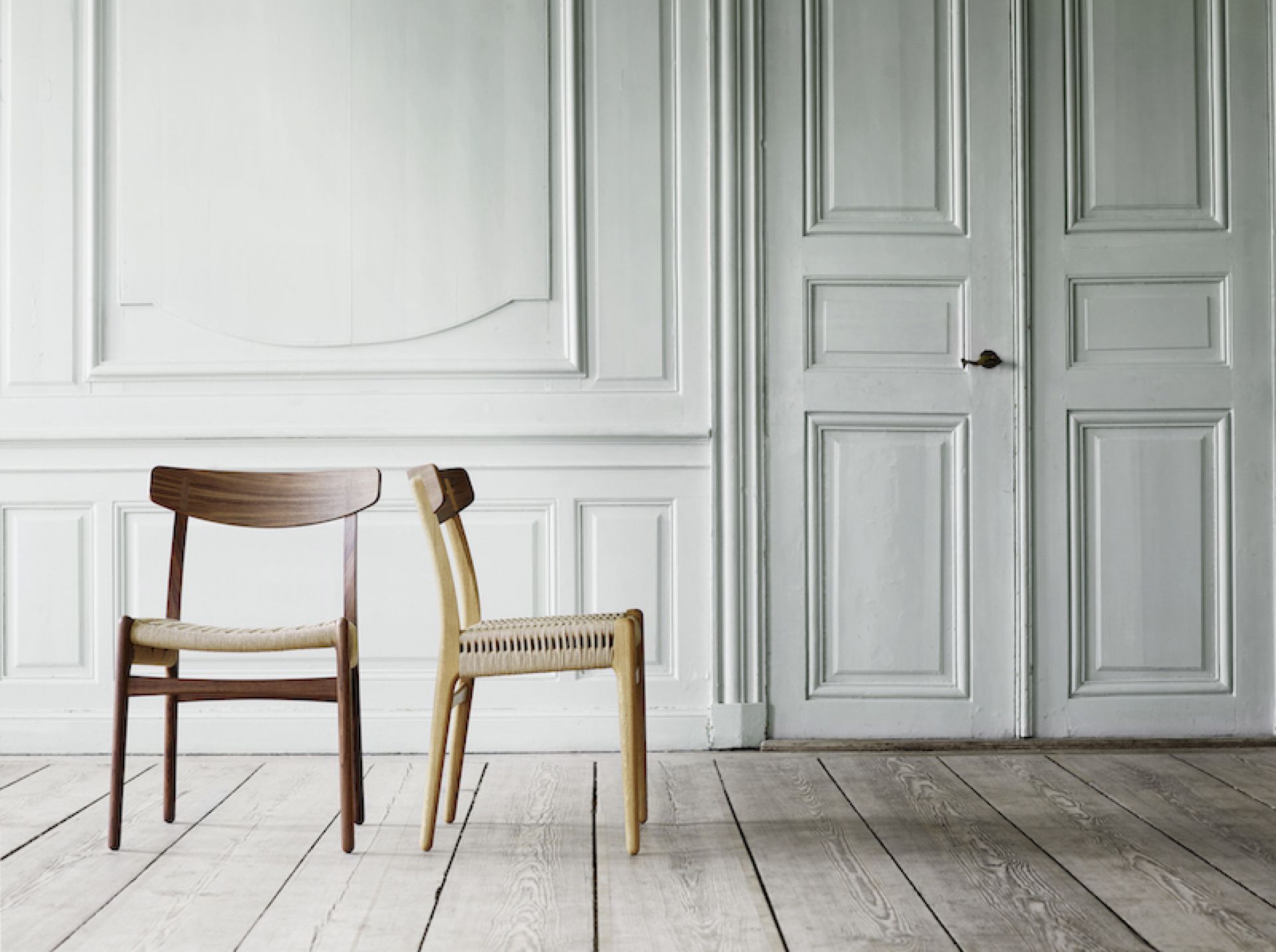 Zwei CH23 Holzstühle von Carl Hansen & Søn mit geflochtenen Sitzen vor weißer Wand.