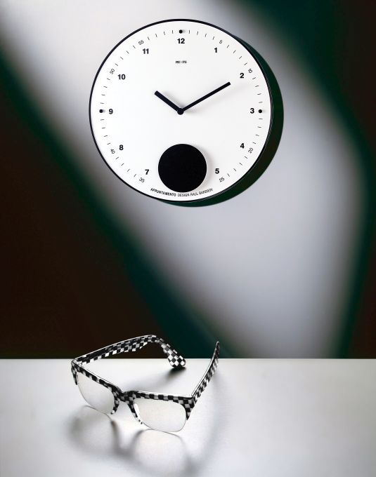Appuntamento Wanduhr Rexite, weiße Designer-Wanduhr mit Pendel und Brille im Schachbrettmuster auf hellem Untergrund.