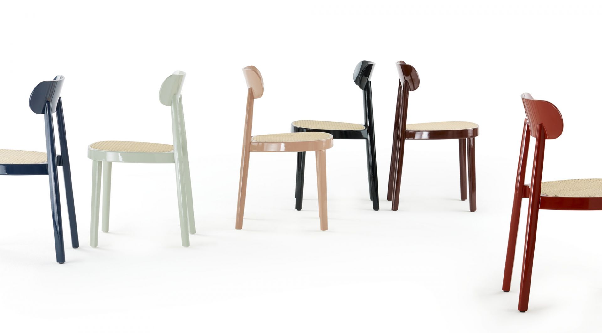 Mehrere Thonet 118 Holzstühle in verschiedenen Farben mit Wiener Geflecht Sitzfläche auf weißem Hintergrund.