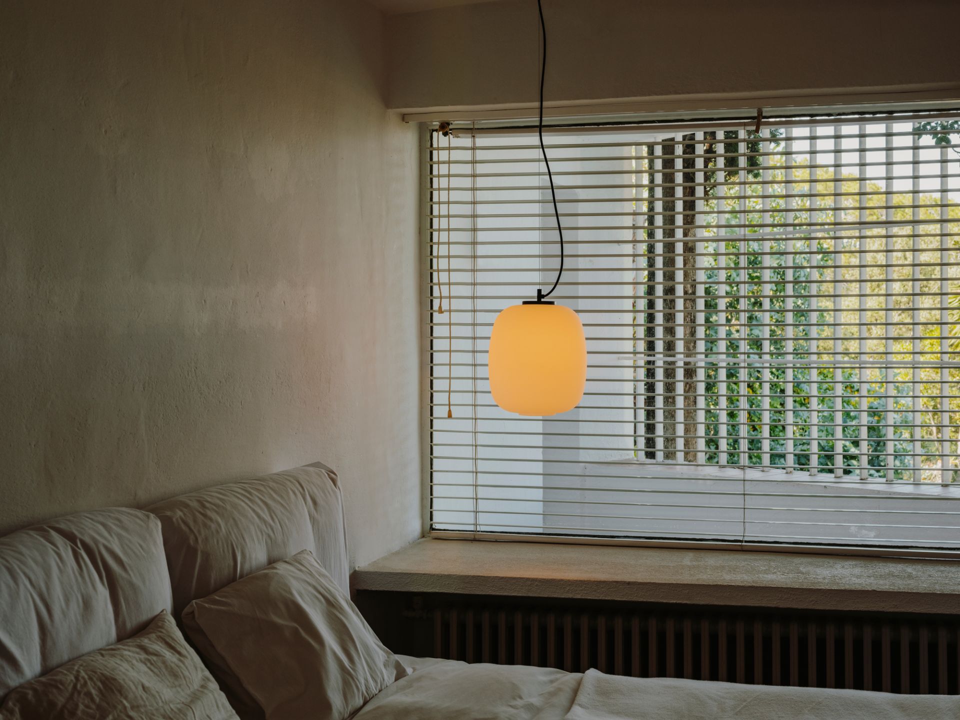 Globo Cesta Pendelleuchte von Santa & Cole über Bett mit Fenster im Hintergrund.