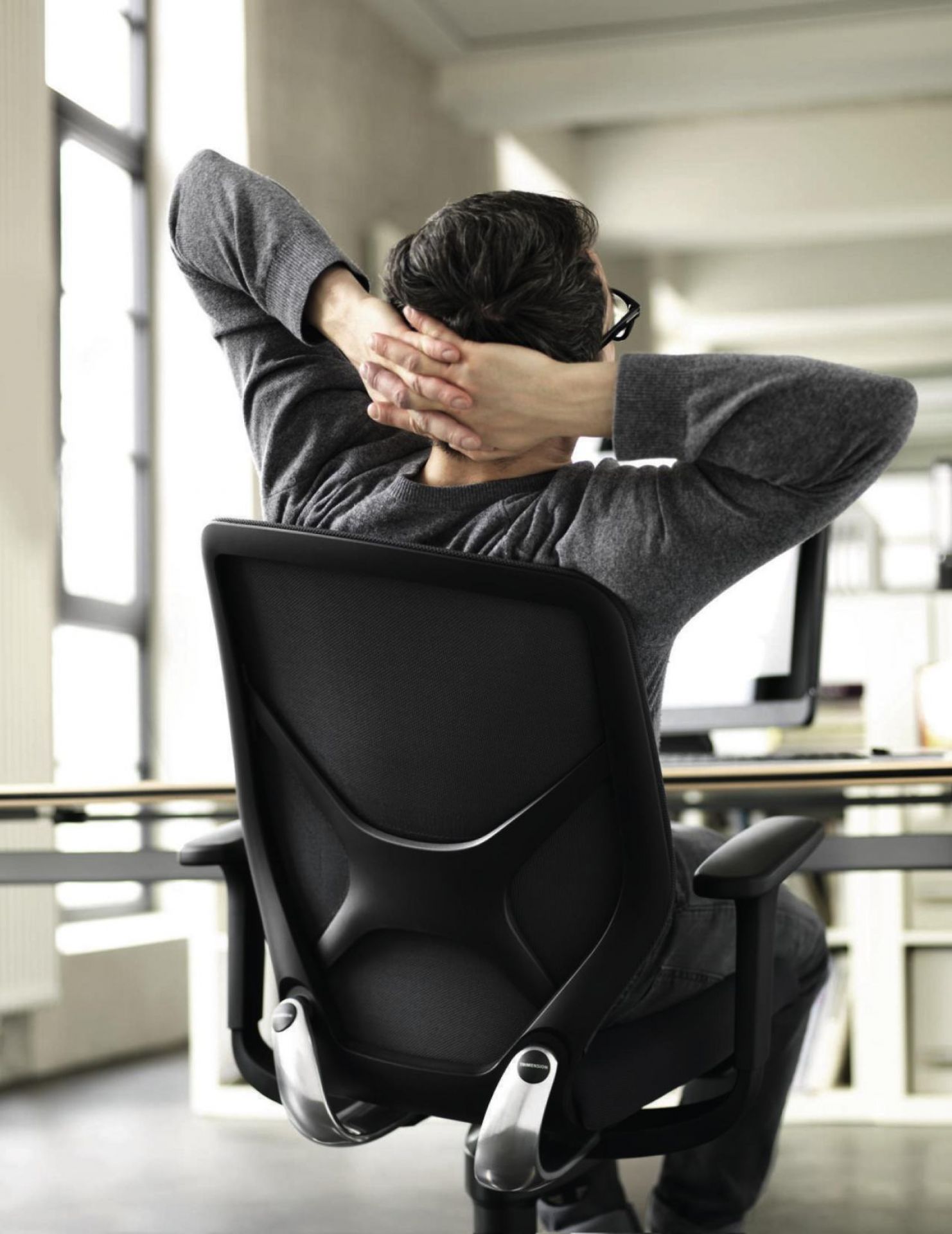 Mann entspannt auf ergonomischem Bürostuhl mit Armlehnen und atmungsaktiver Rückenlehne im modernen Büro.