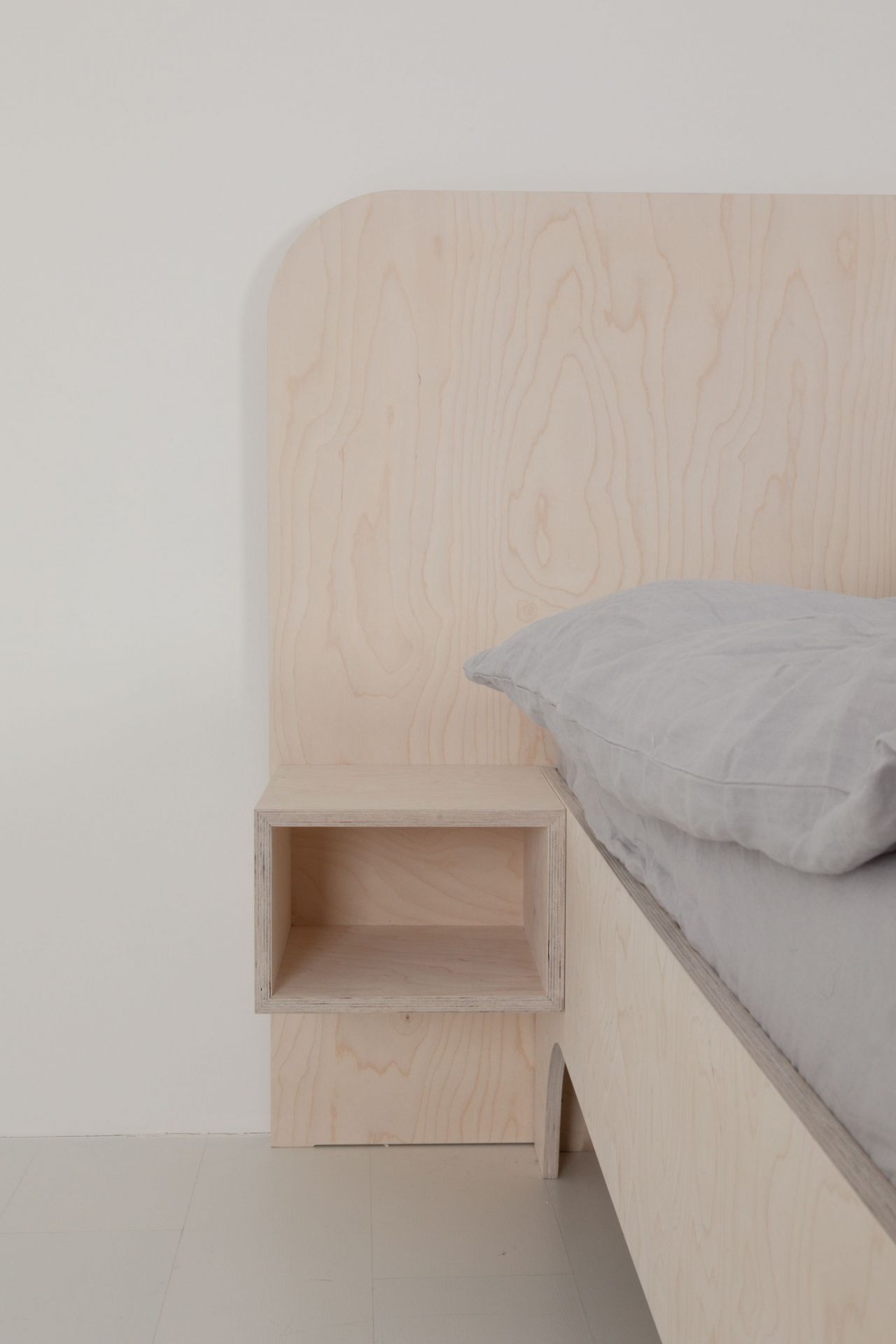 VALENTINA Bett aus hellem Holz mit integriertem Nachttisch und grauem Kissen.