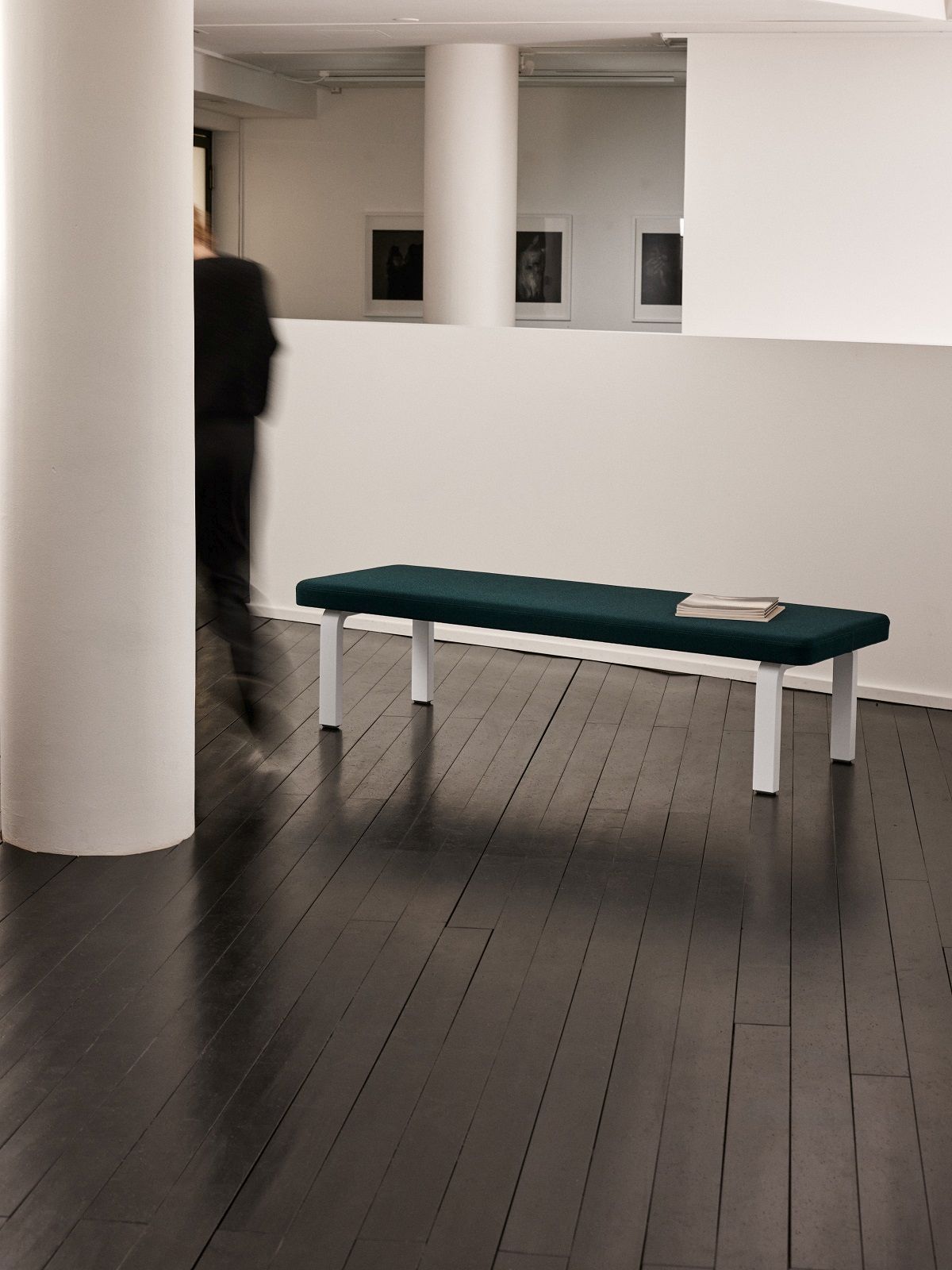 Bench 167 Bank von Artek mit dunkelgrünem Sitzpolster und weißen Beinen auf dunklem Holzboden.
