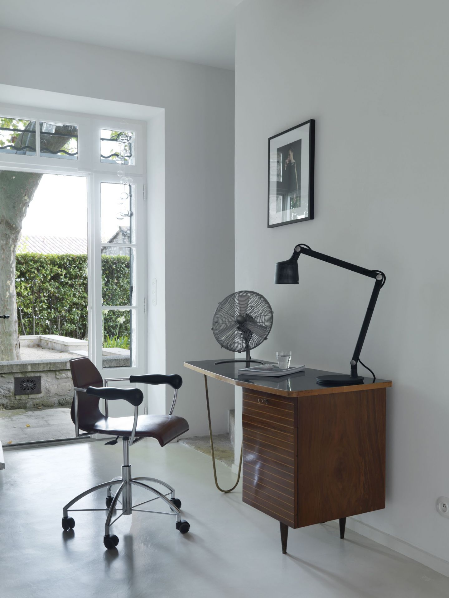 Schwarze Vipp Tischlampe auf Schreibtisch mit Ventilator und Bürostuhl in modernem, hellen Arbeitszimmer.