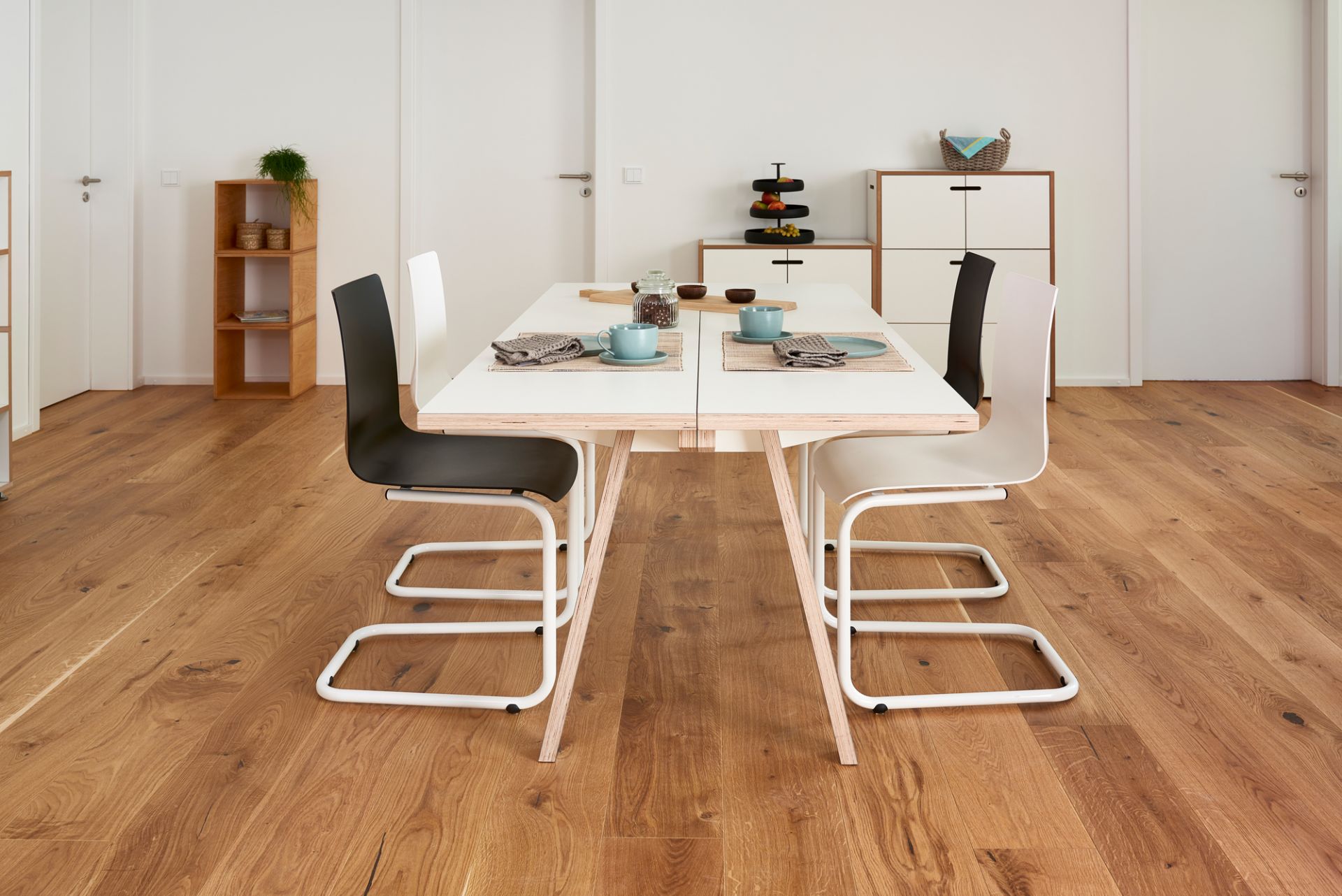 Tojo Steck Tisch aus Holz mit weißer Tischplatte und schwarzen und weißen Stühlen.