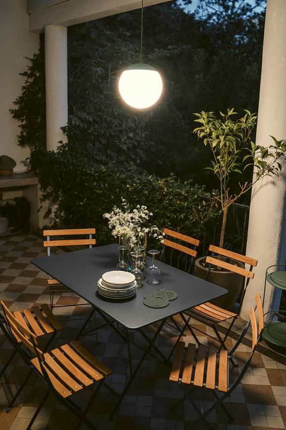 Außenbereich mit Esstisch und Stühlen, beleuchtet durch eine moderne Mooon Pendelleuchte von Fermob.