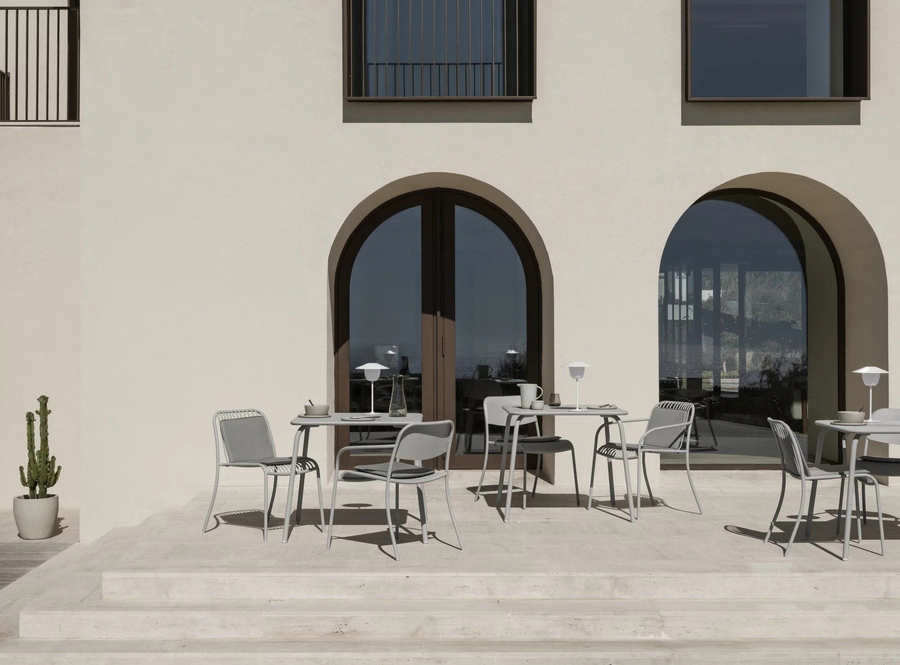 Blomus Yua Armlehnstuhl Outdoor auf Terrasse mit Tischen und Lampen, modernes Gartendesign.