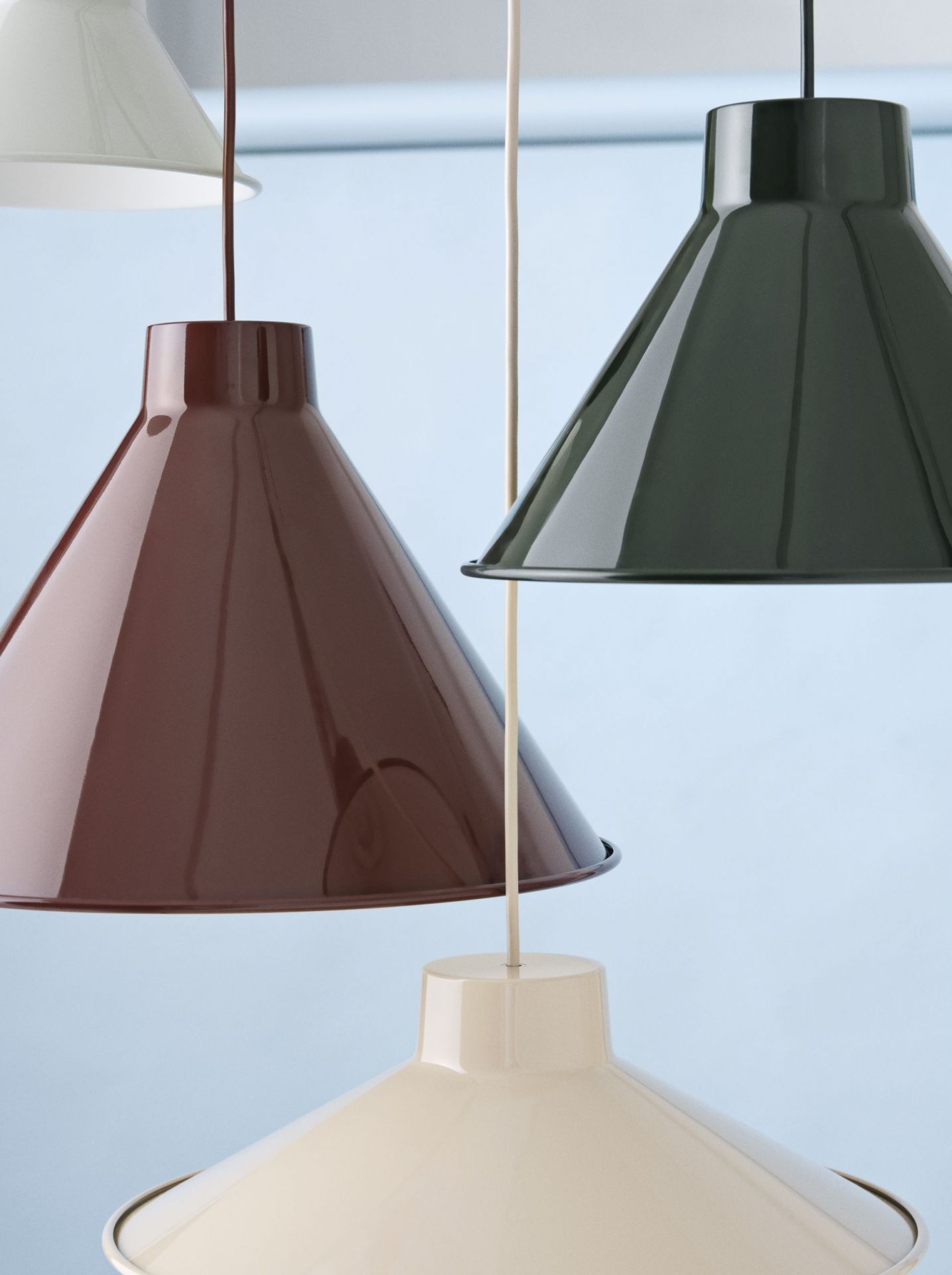 Nahaufnahme von mehreren Muuto Top Pendelleuchten in Grau, Braun und Creme vor blauem Hintergrund.