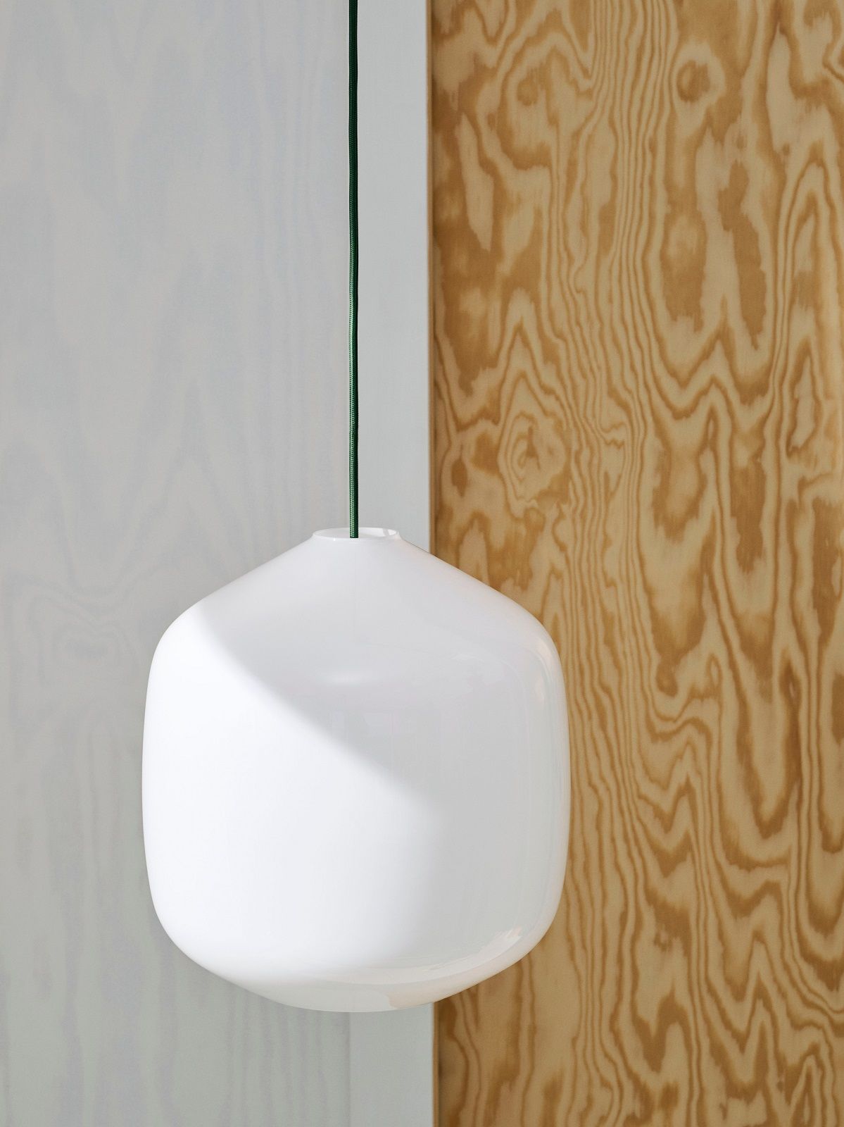 Nahaufnahme der weißen Aspekt Buoy Glas Pendelleuchte von Hay mit grünem Kabel vor Holzwand.