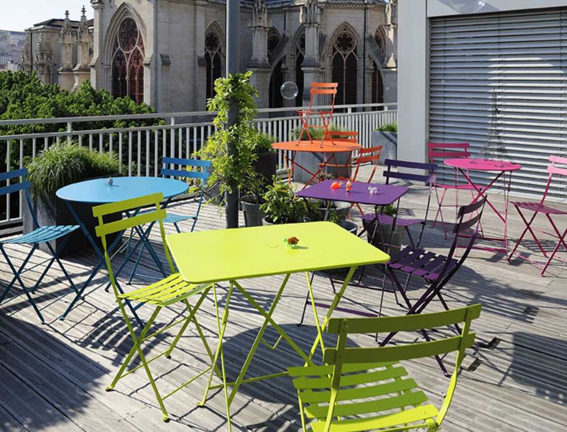 Bunte Fermob Bistro Gartenmöbel auf einer Dachterrasse mit Tischen und Stühlen in verschiedenen Farben.