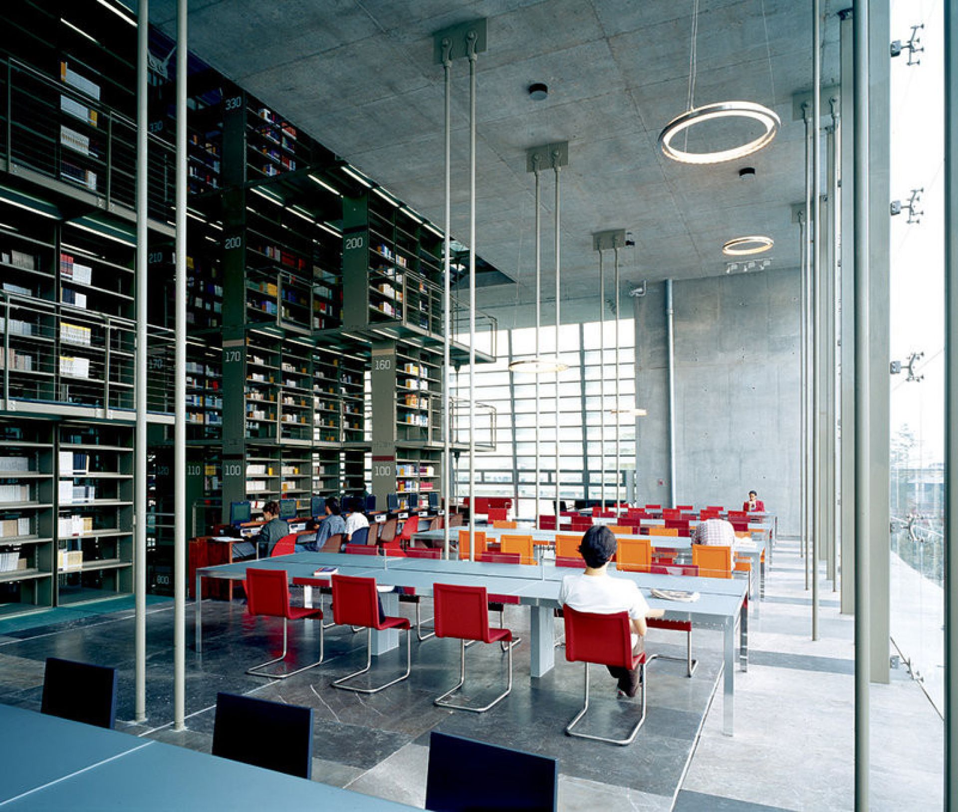 Innenaufnahme einer Bibliothek mit roten Vitra .05 Stühlen an langen Tischen unter Regalen.