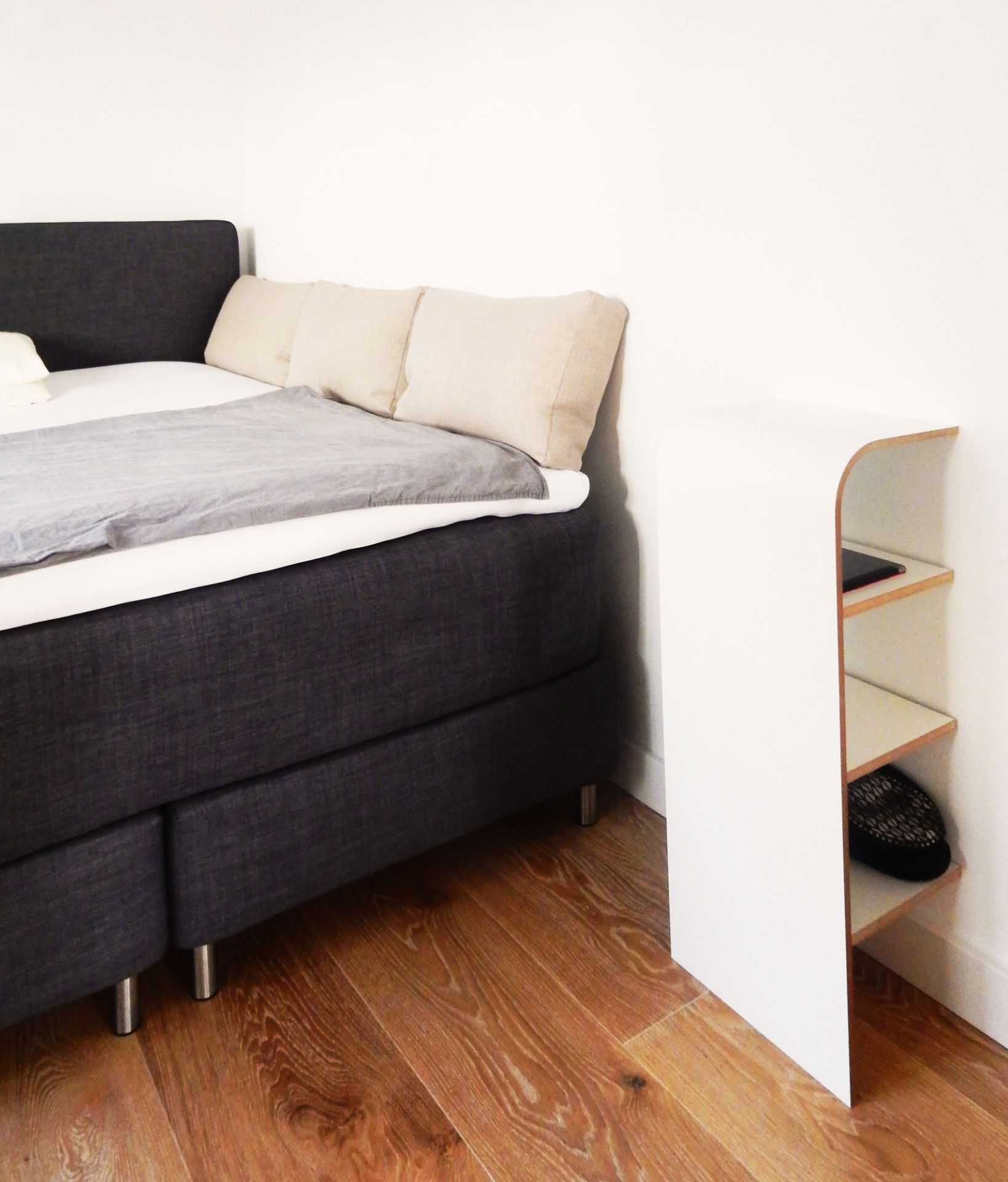 Tojo Schuhregal aus weißem Holz neben einem Bett im Schlafzimmer, minimalistisches Design.