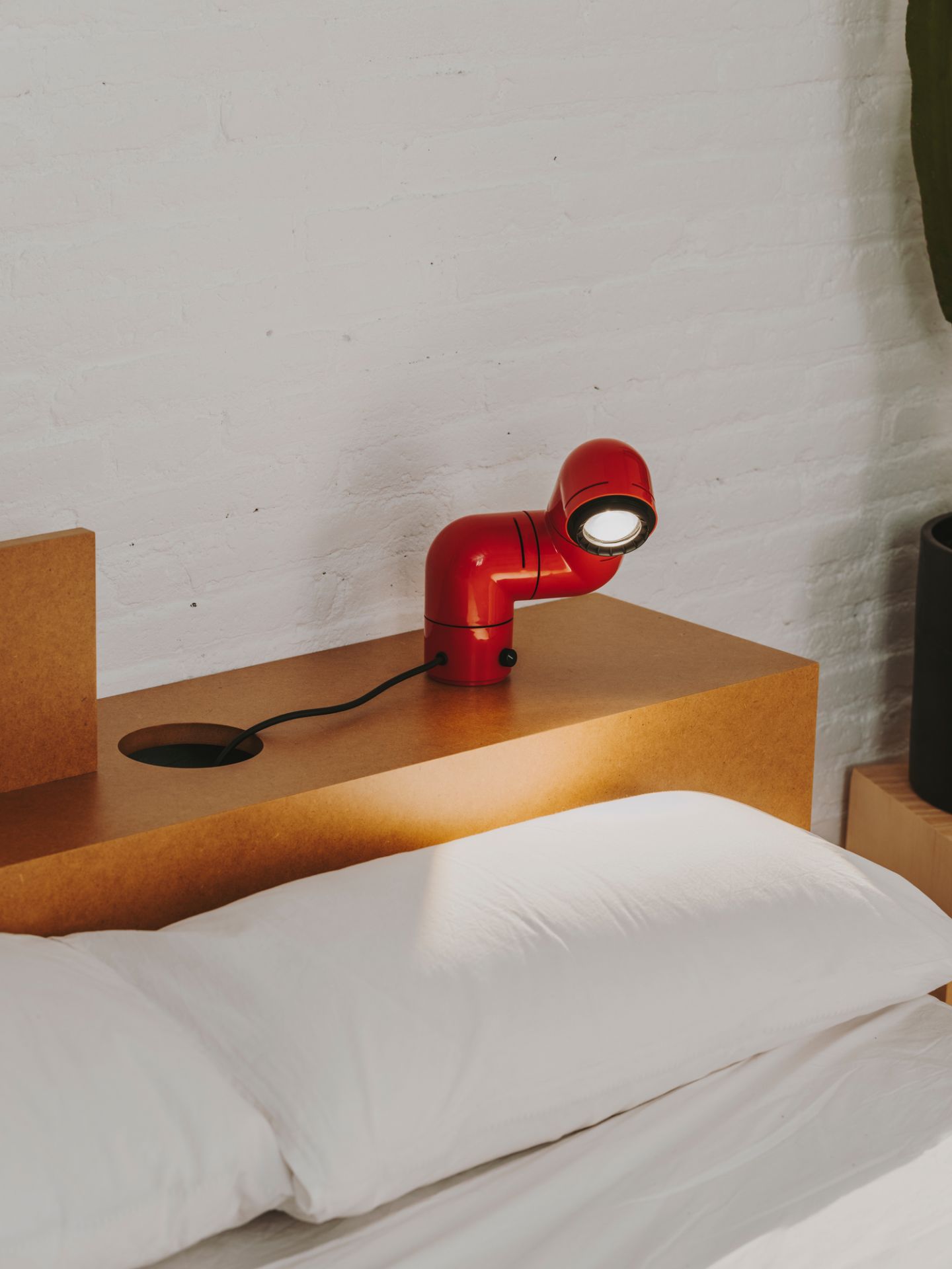 Rote Tatu Tischleuchte von Santa & Cole auf Nachttisch neben einem Bett mit weißem Kissen.