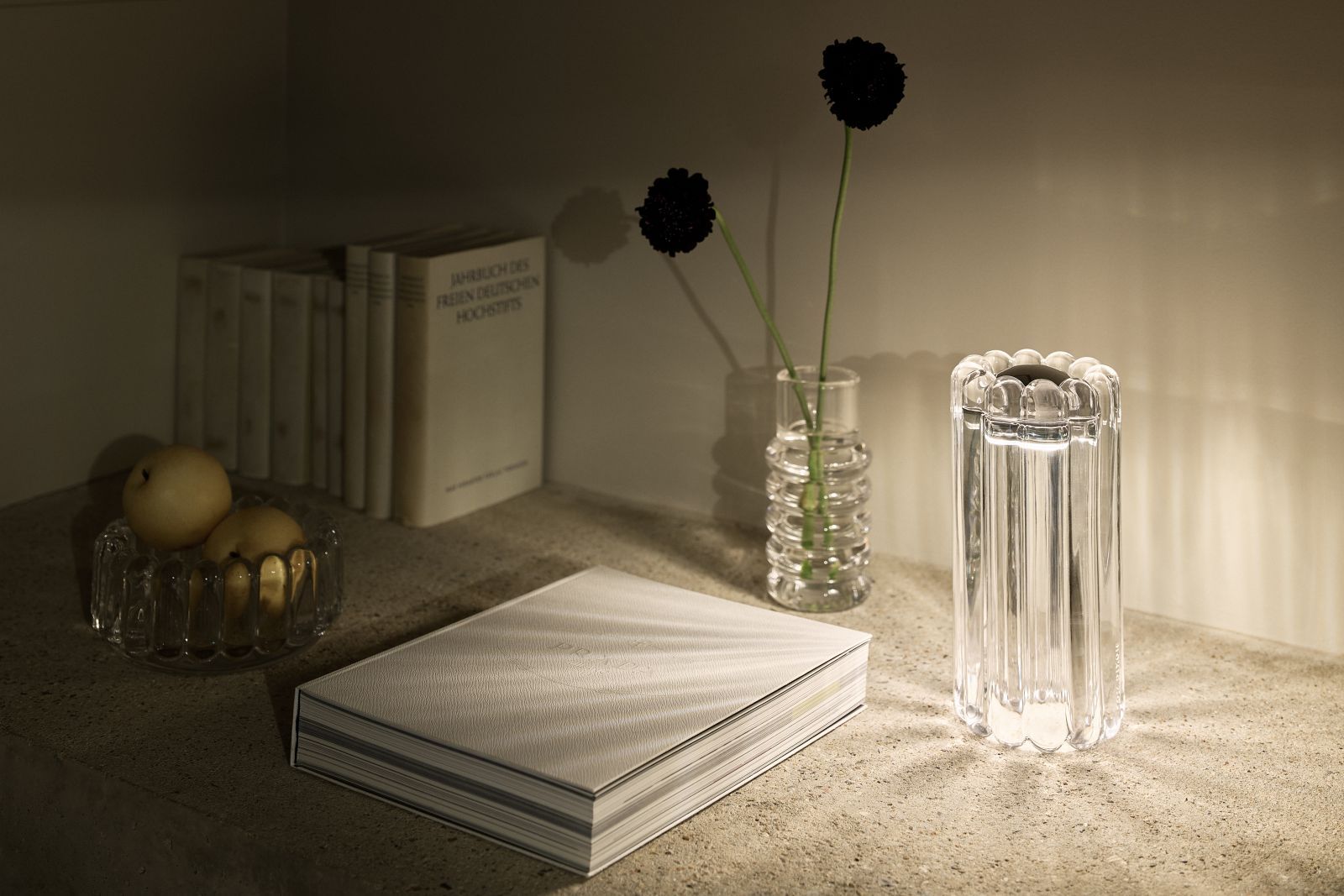 Nahaufnahme der Tom Dixon Press Tischleuchte aus geriffeltem Klarglas, neben Buch und Vase.