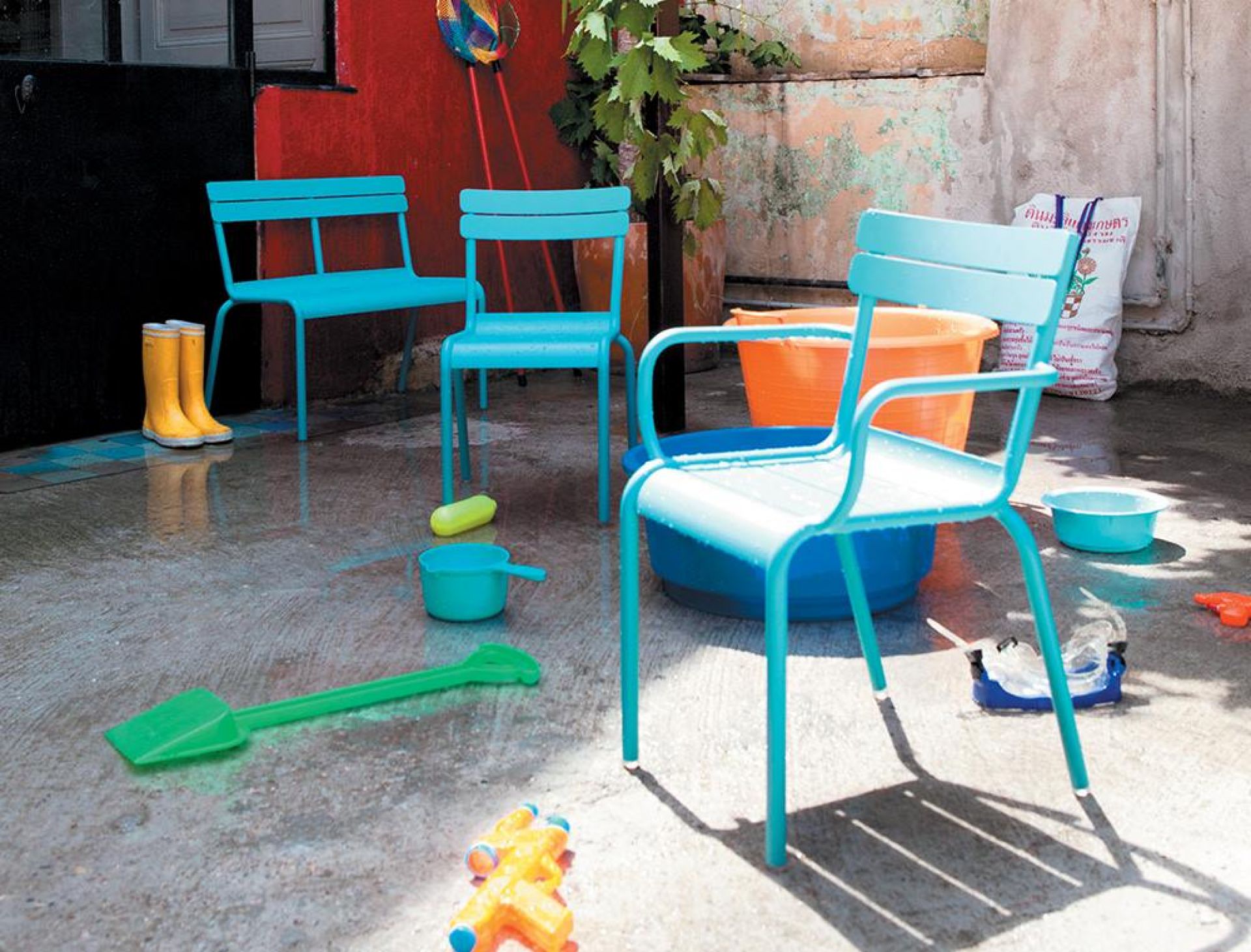 Blauer Luxembourg Kinderstuhl von Fermob im Außenbereich mit Spielzeug und Gummistiefeln.