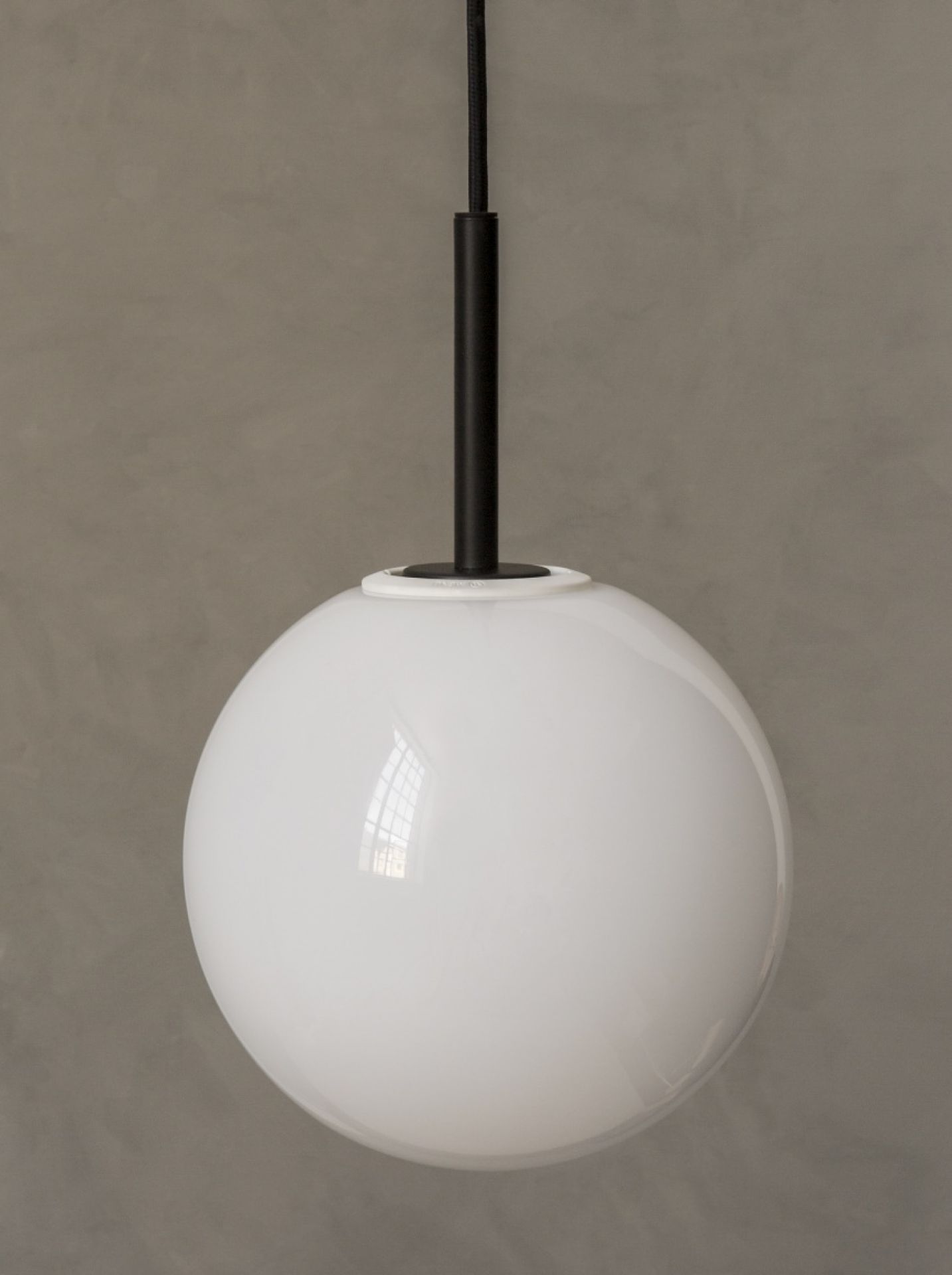 Nahaufnahme der Audo TR Bulb Pendelleuchte mit weißem Opalglas-Diffusor und schwarzer Aufhängung vor grauer Wand.