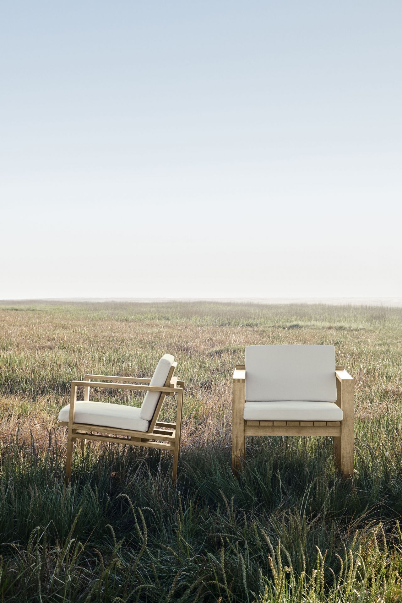 Zwei Bodil Kjaer Sessel Outdoor von Carl Hansen & Søn aus Teakholz mit weißen Polstern im Gras.