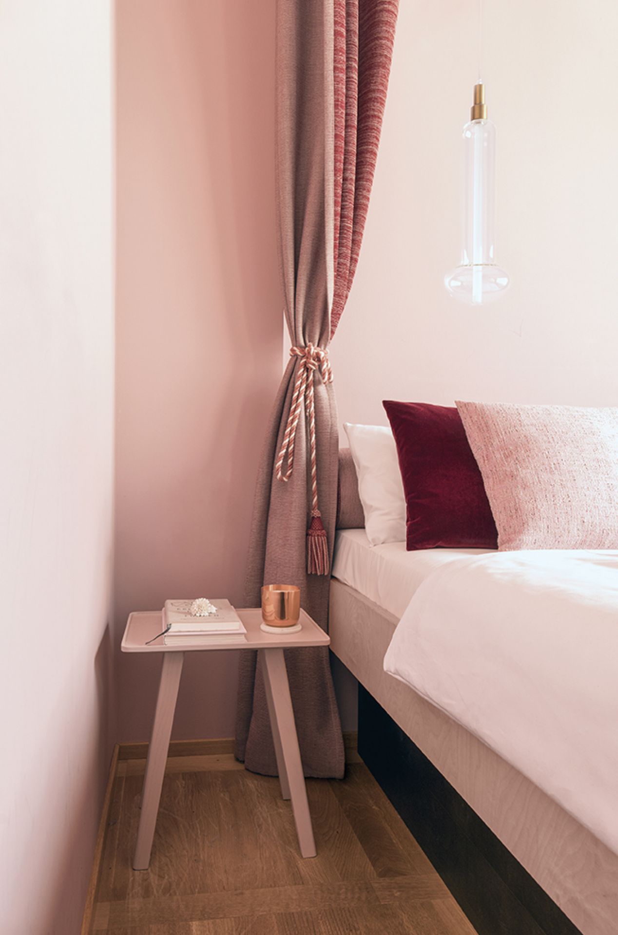 Nini Hocker von Schönbuch in Rosa als Nachttisch neben einem Bett mit Kissen.