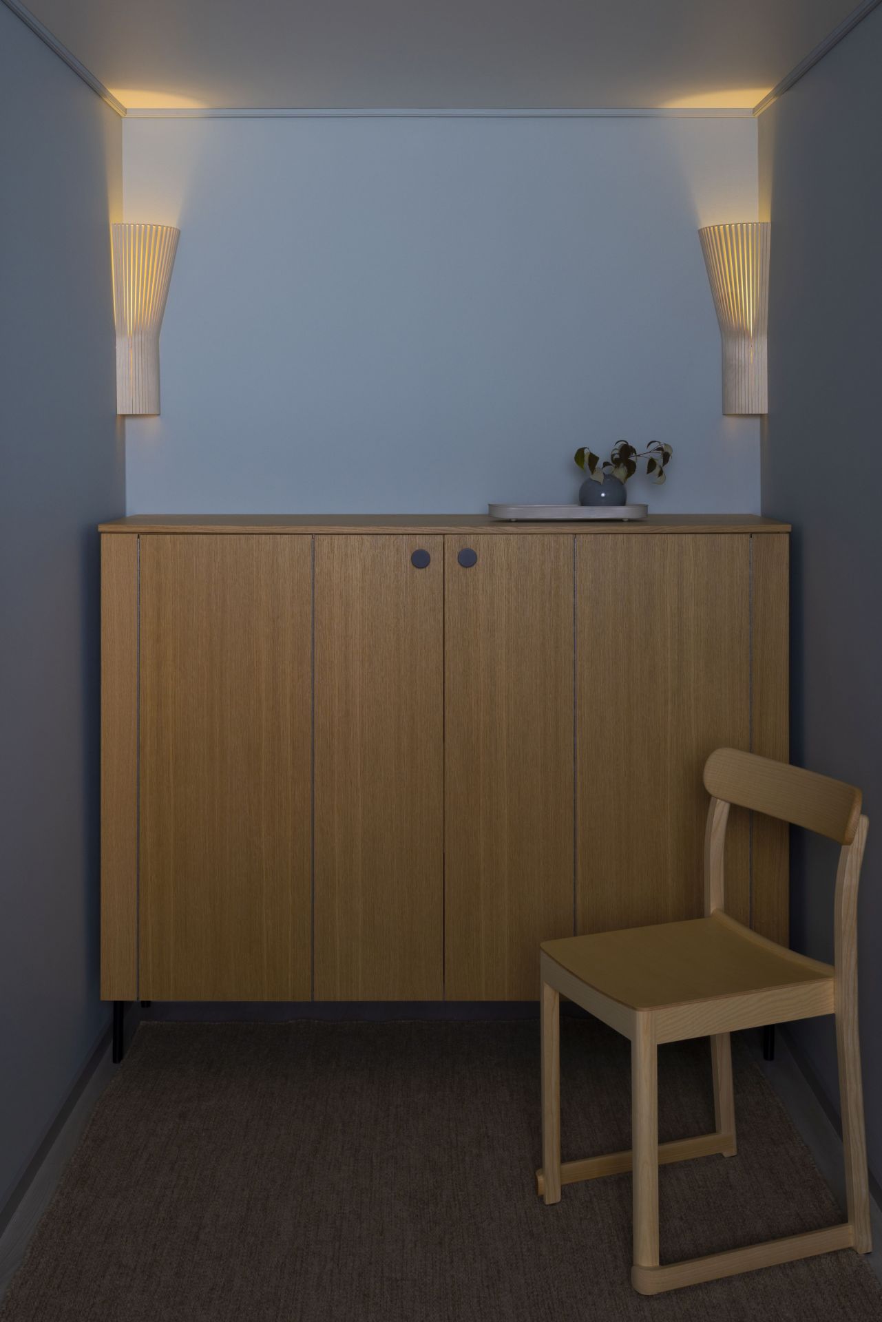 Secto Design 4237 Eckleuchte aus Birkenholz, montiert in einer Ecke über einem Holzschrank mit Stuhl.