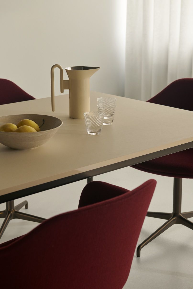 AndTradition Drip Table HW58 mit Krug, Gläsern, Obstschale und roten Stühlen in minimalistischem Interieur.