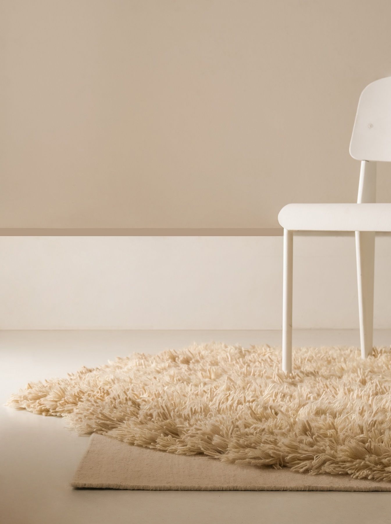 Detailansicht: Beige Alga Teppich von Nanimarquina mit weißem Stuhl auf hellem Untergrund. Hochfloriger Teppich.