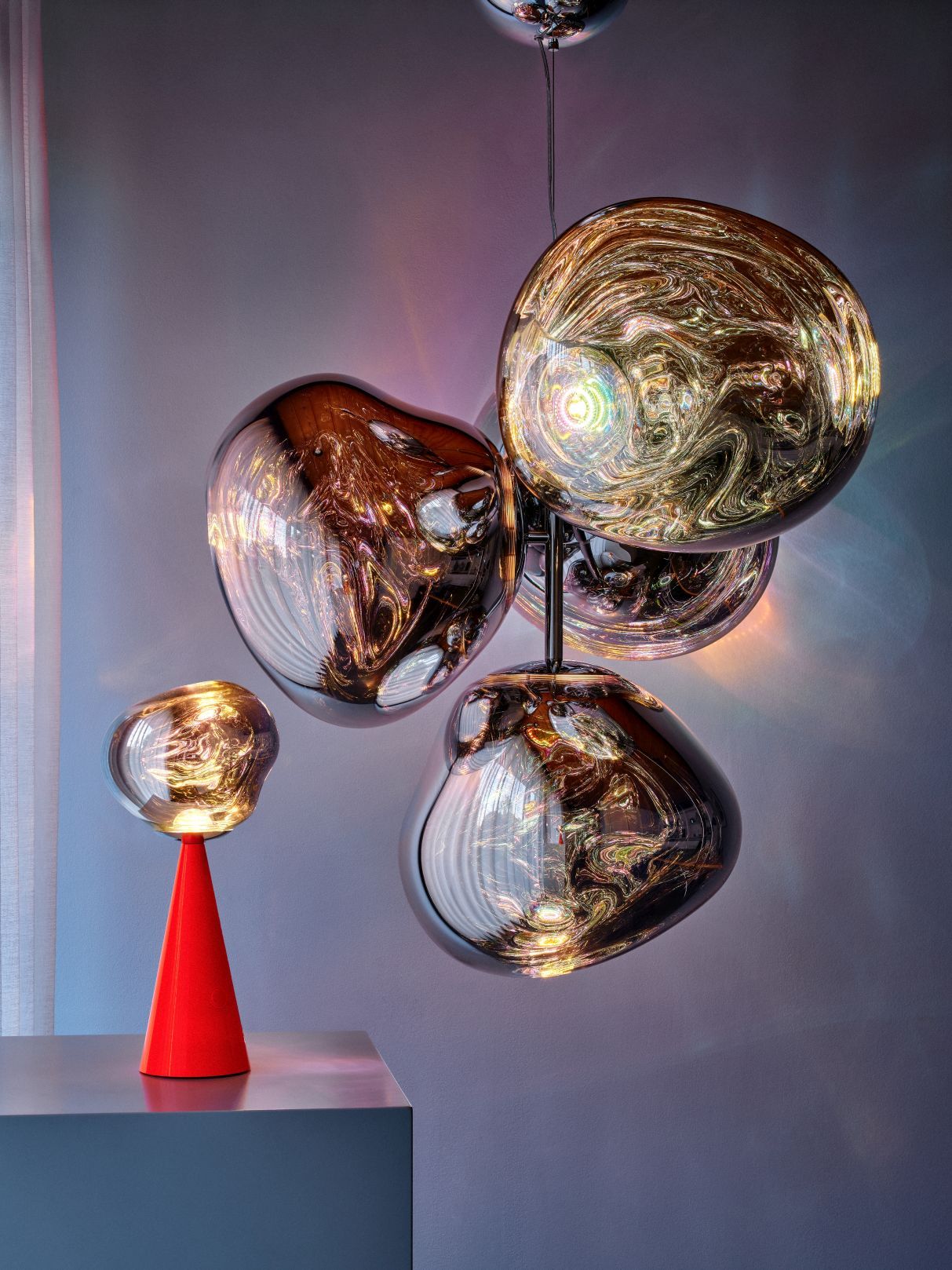 Tom Dixon Melt Leuchten: Pendelleuchte mit vier Lampenschirmen und rote Melt Tischleuchte auf einem Tisch.